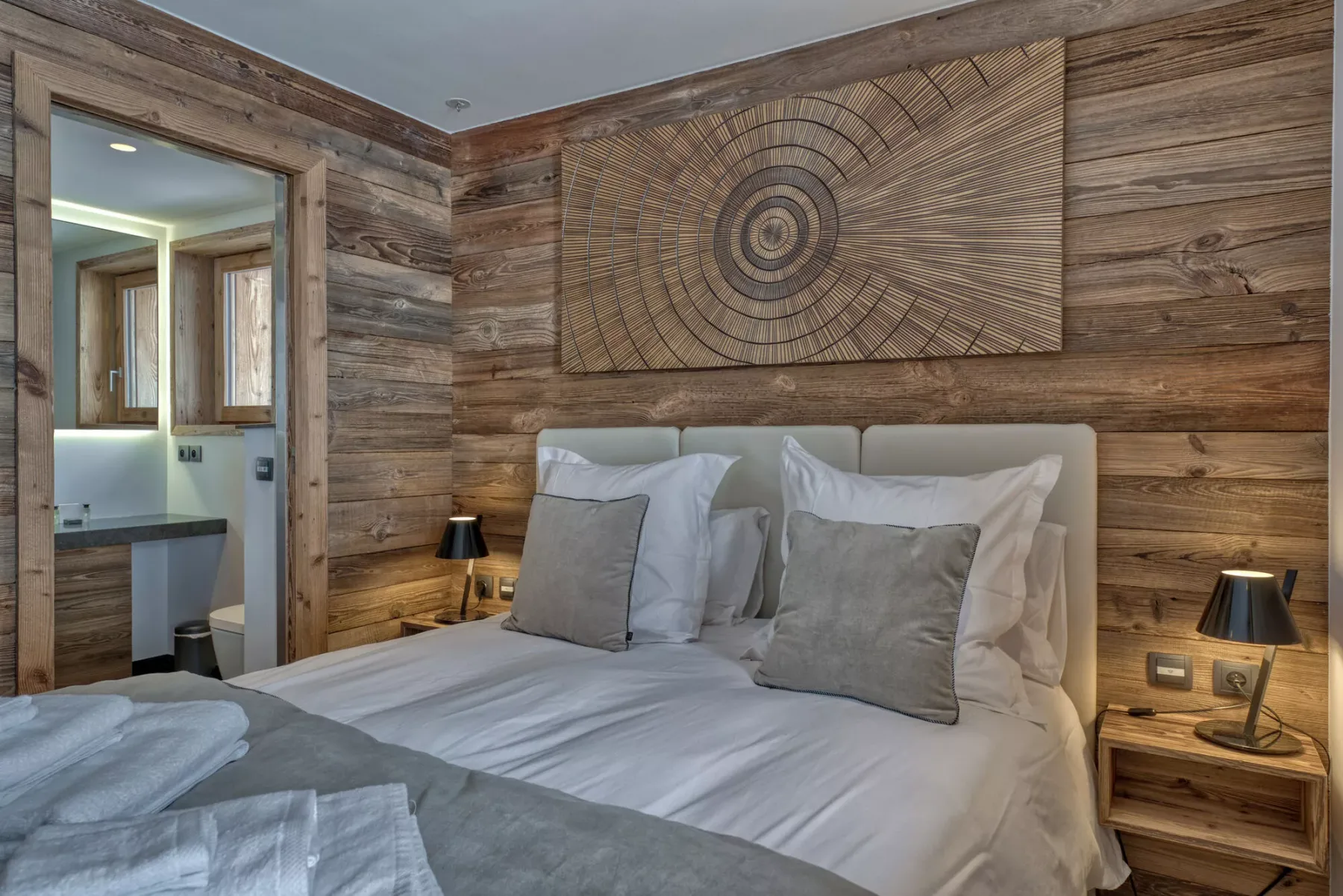 A bedroom with a neatly made bed and a large circular wall artwork.