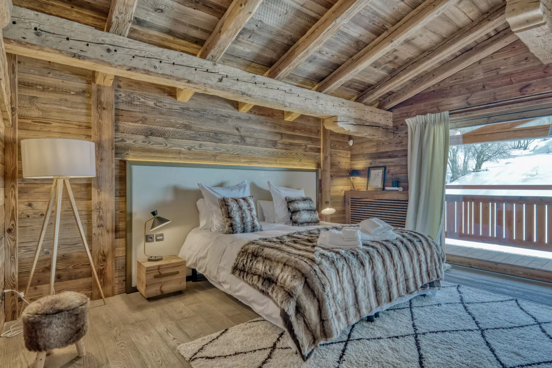 A rustic bedroom with a large bed and a window overlooking snowy trees.