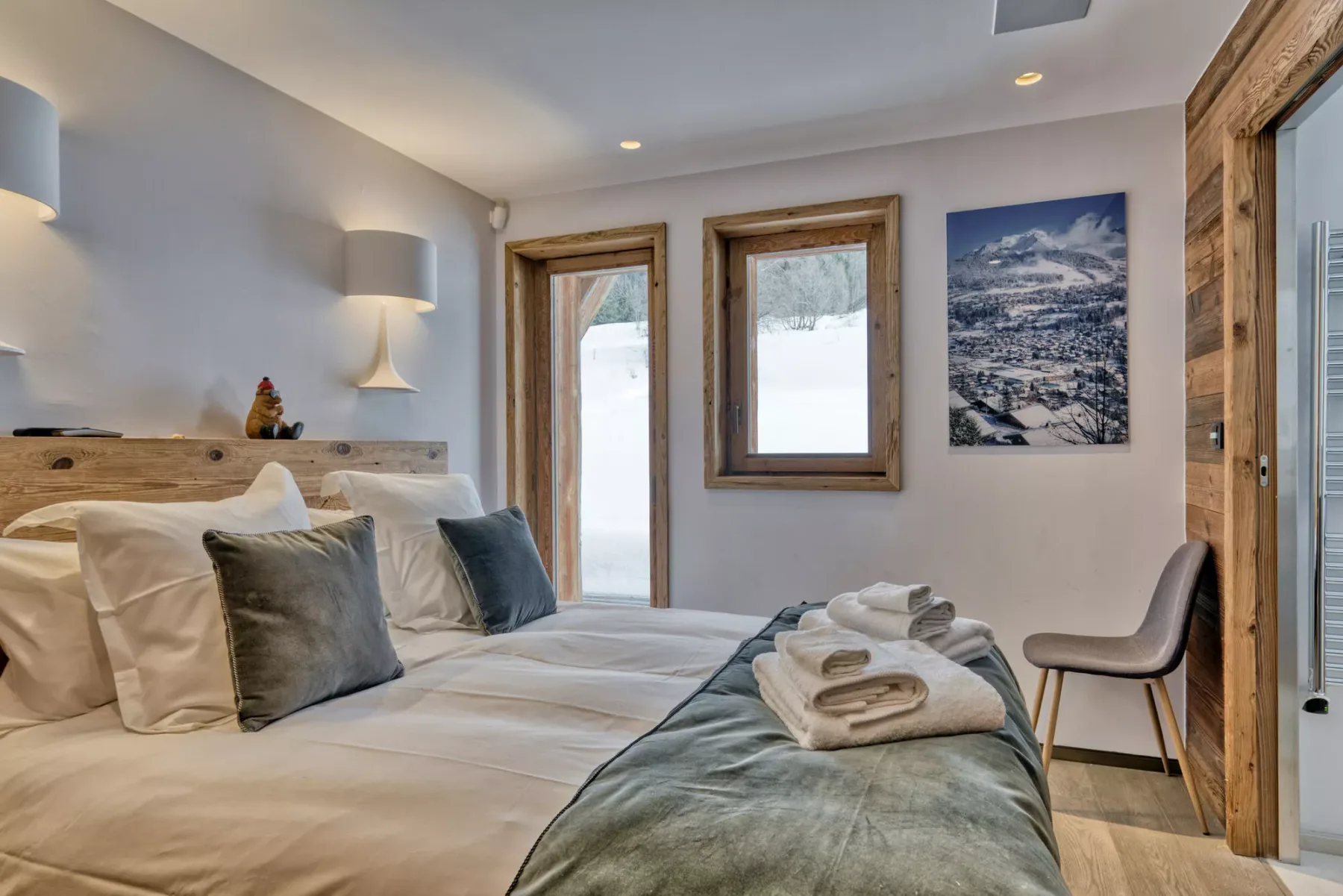 A bedroom with neatly made beds, folded towels, and windows overlooking snowy scenery.