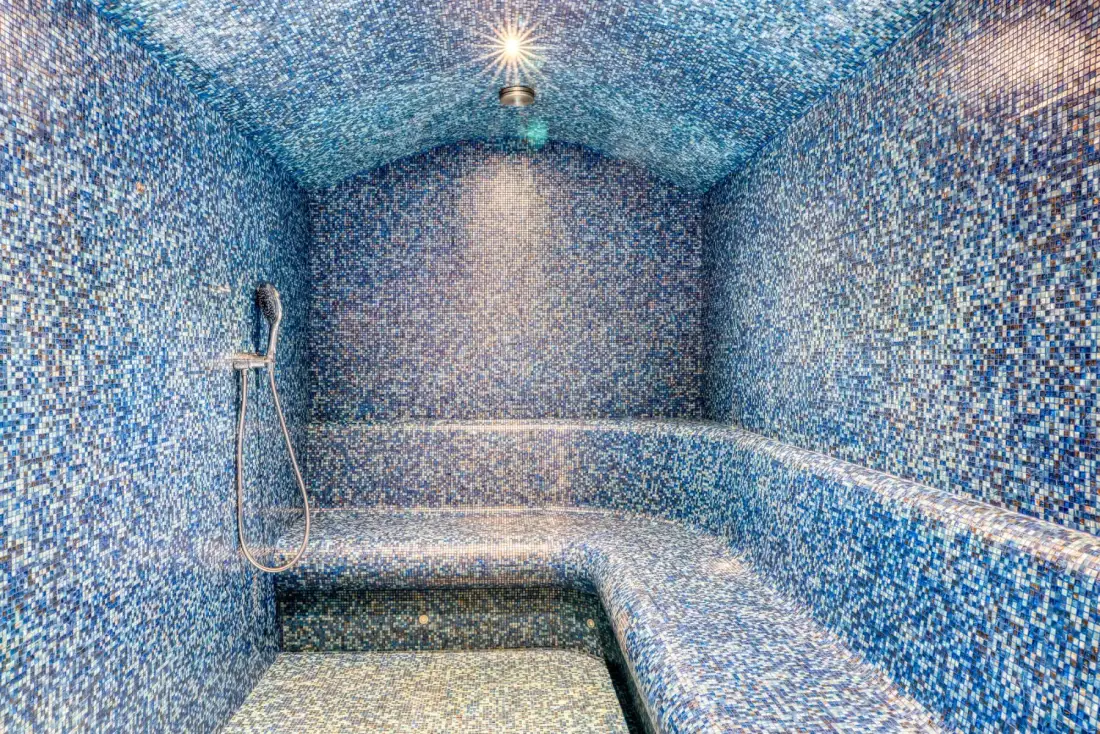 A tiled steam room with a built-in bench and wall-mounted shower.