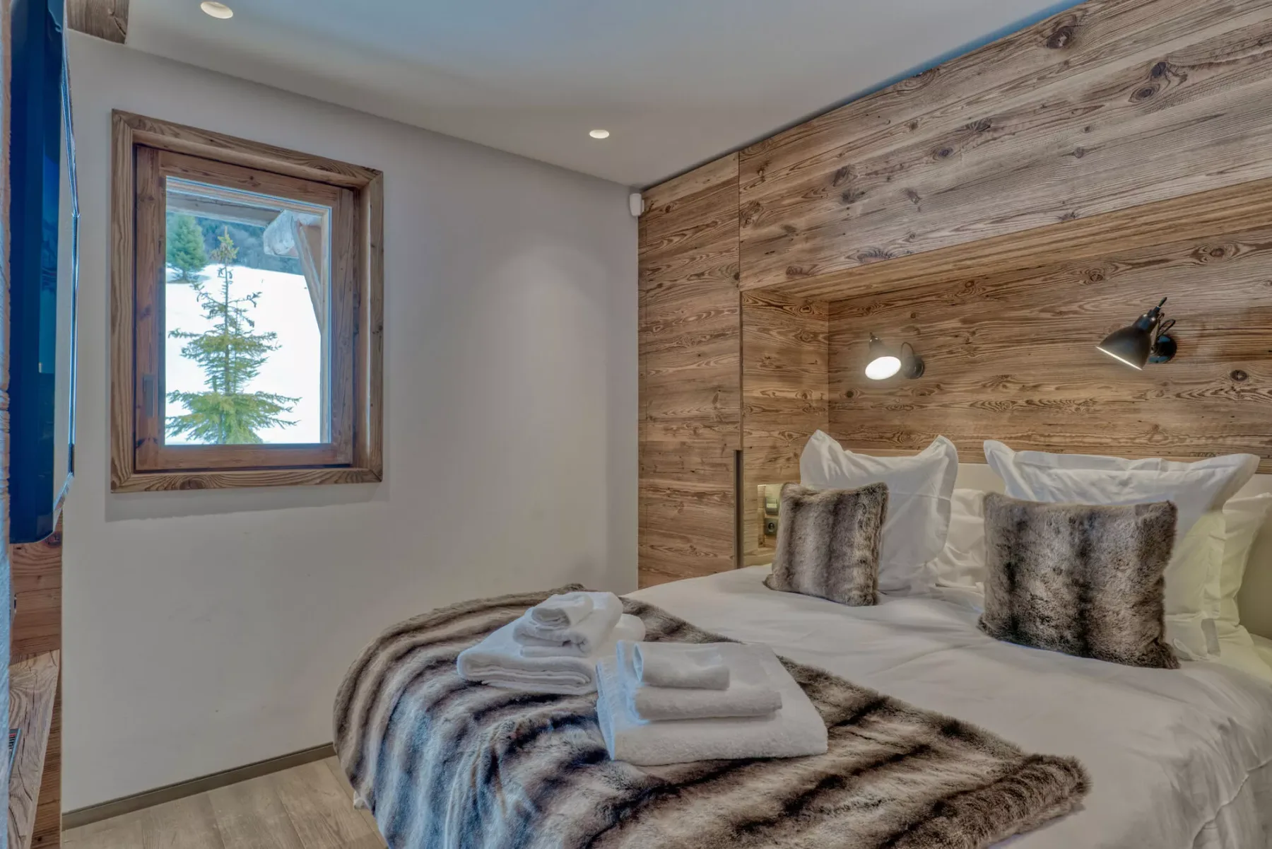 A bedroom with a bed dressed in white linens and a wood-paneled wall.