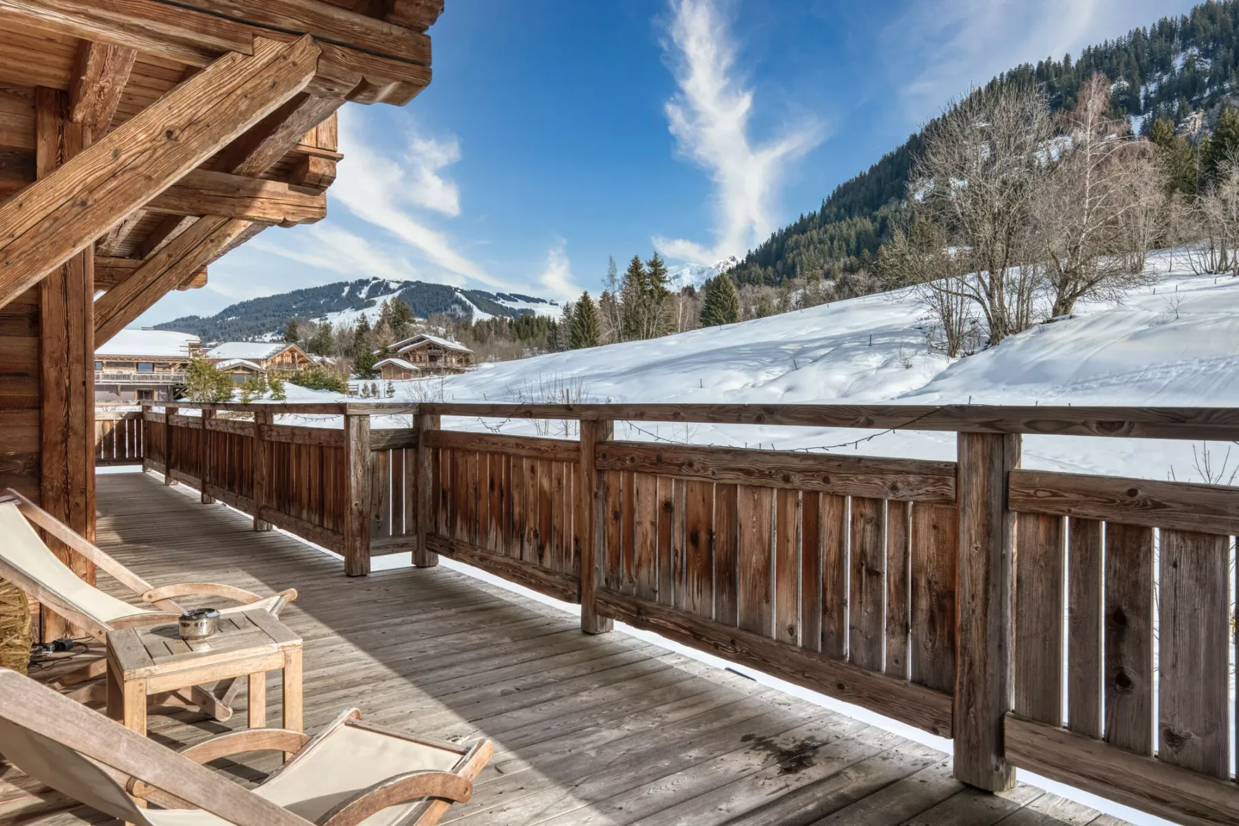 A wooden balcony overlooks a snowy mountain slope, with seating beside the railing.