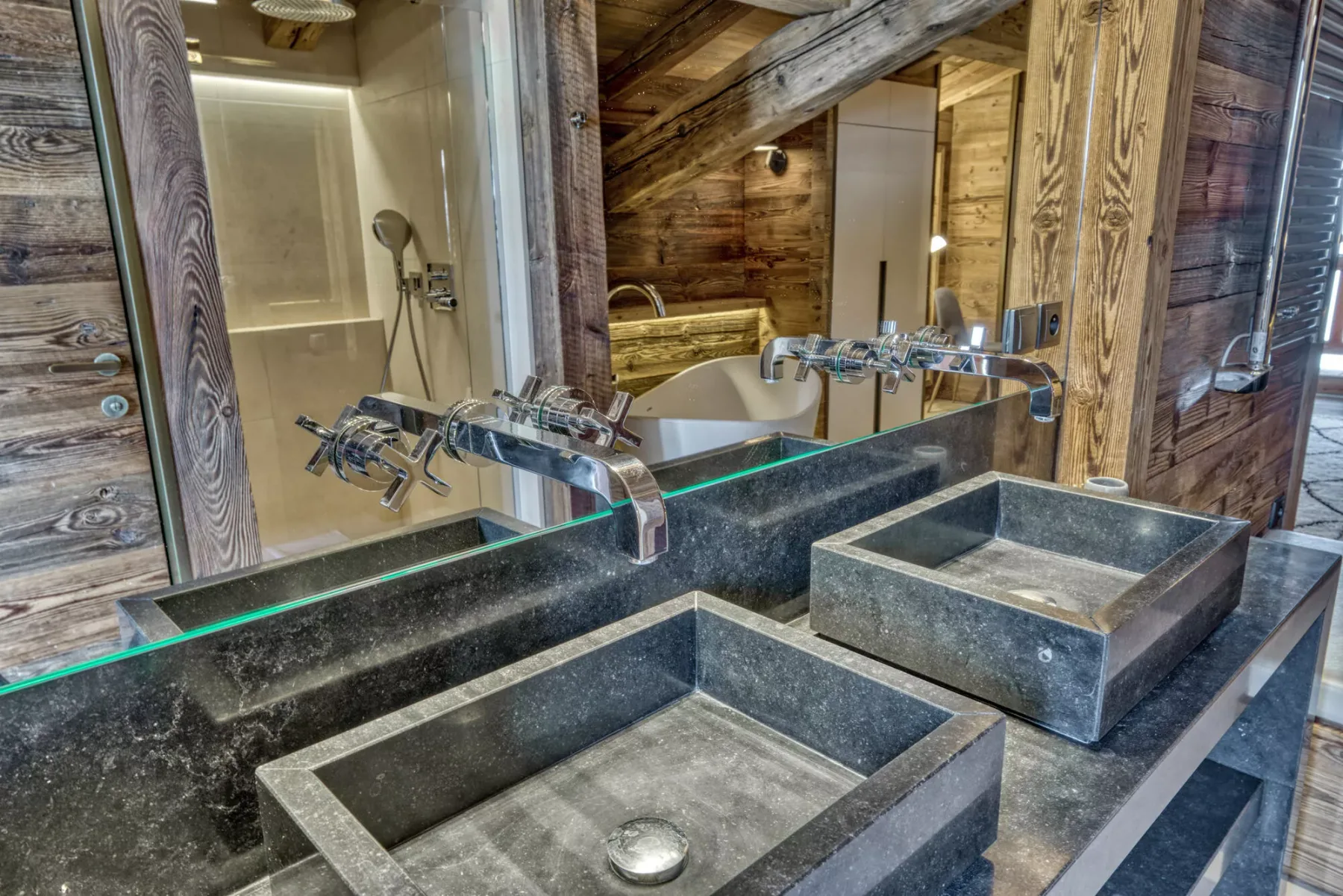 A rustic bathroom features dark stone sinks and a glass-enclosed shower.