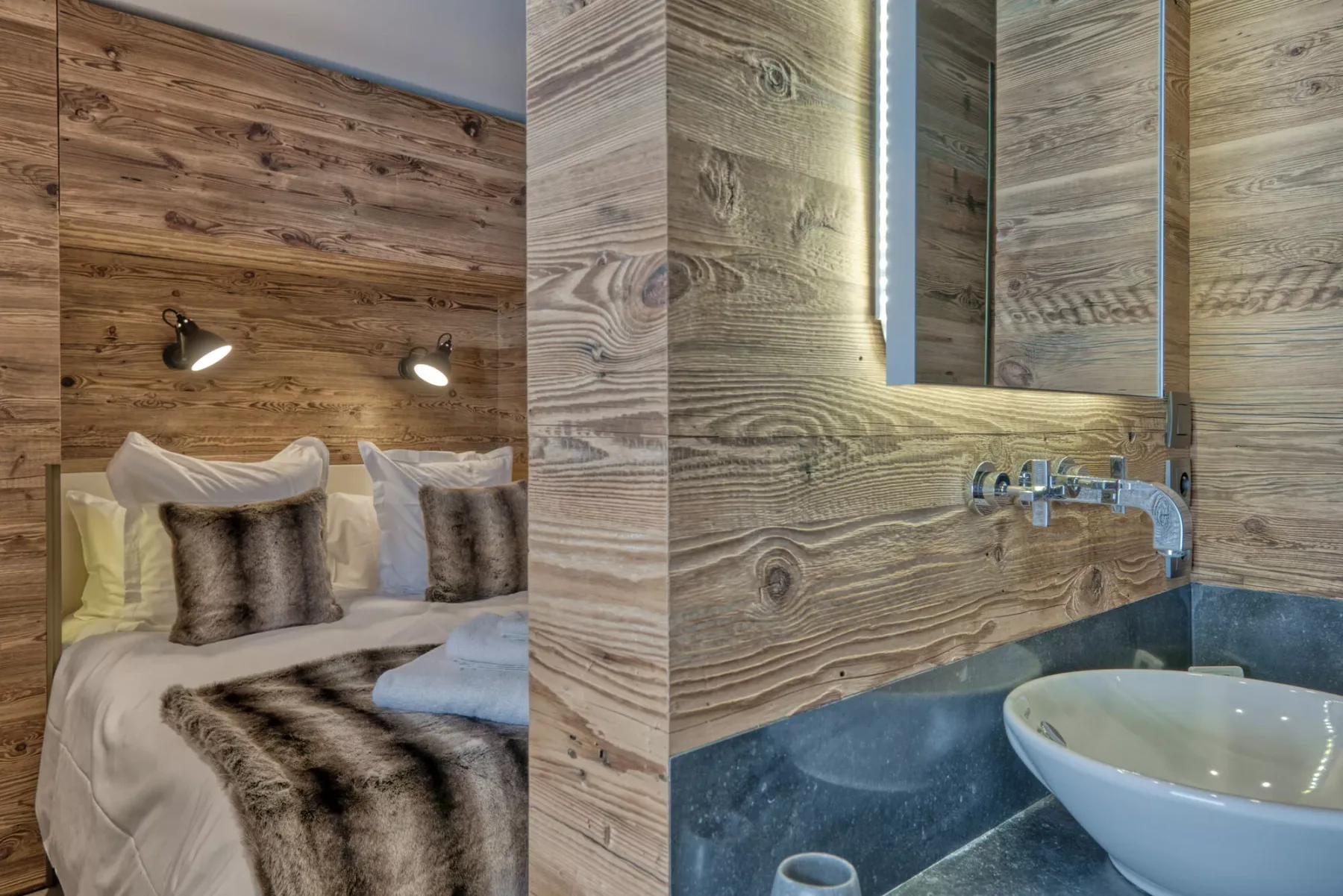 A bedroom with a neatly made bed beside a vanity and sink.