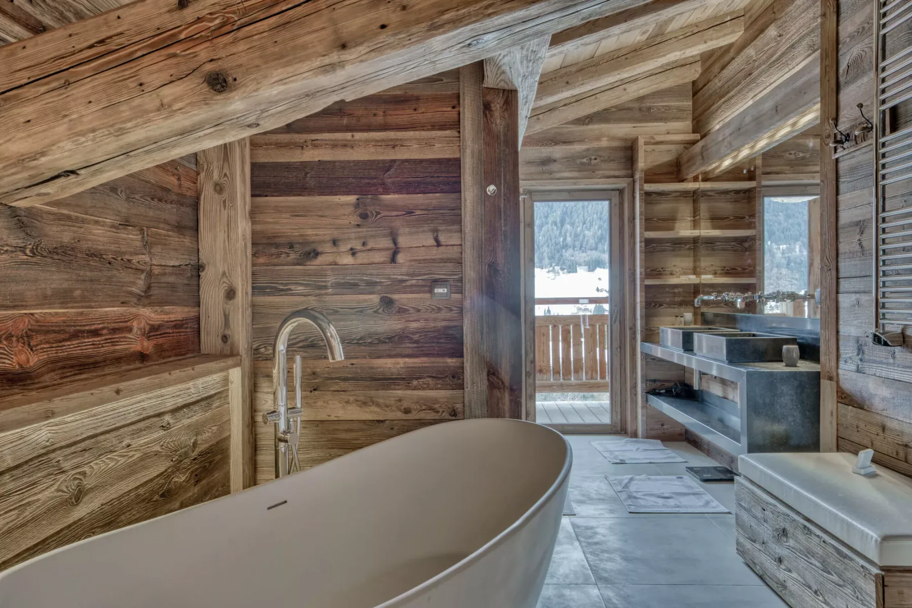 A rustic bathroom features a freestanding bathtub beside a sink and windows.