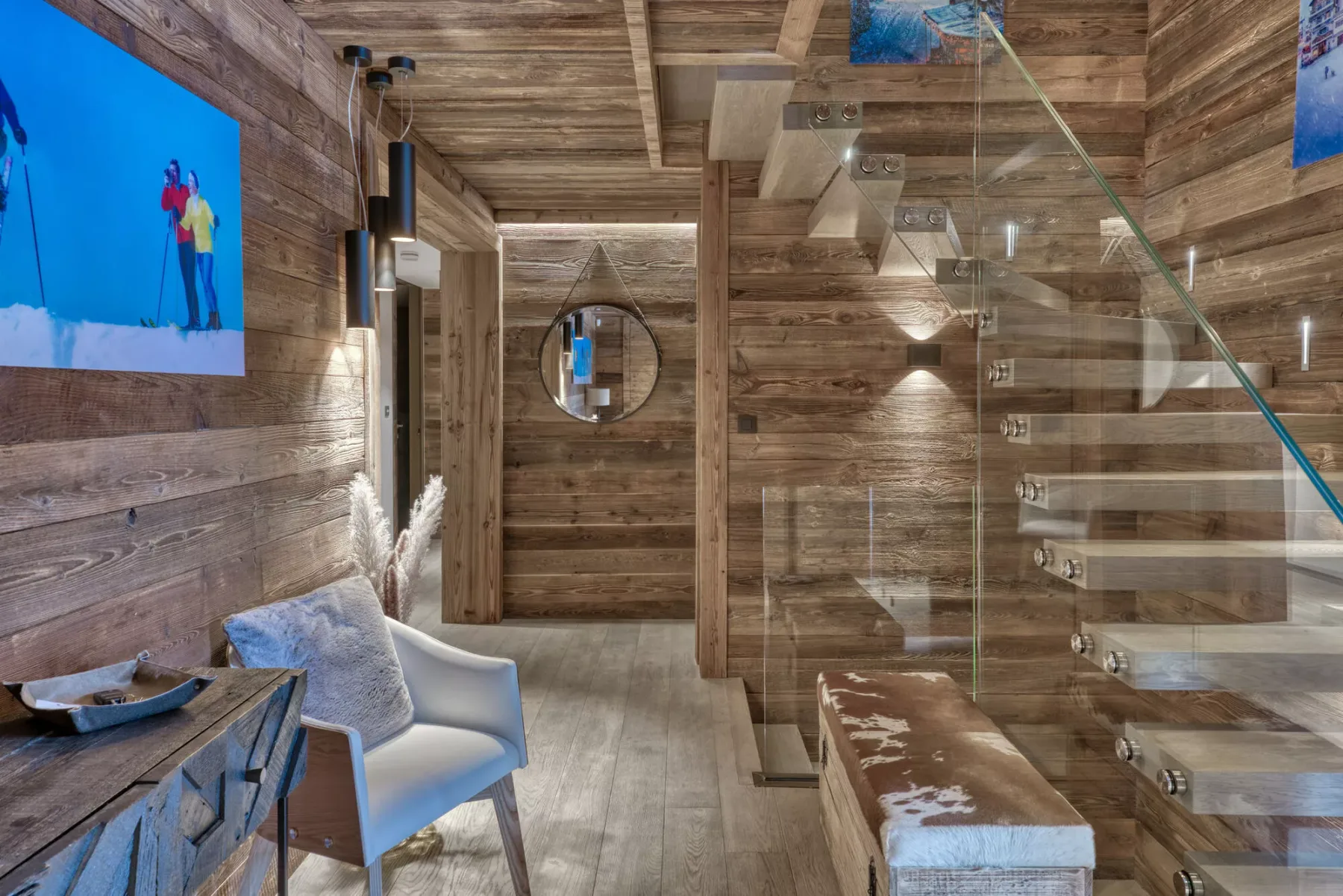 Una habitación revestida de madera tiene una escalera de vidrio y una silla clara.