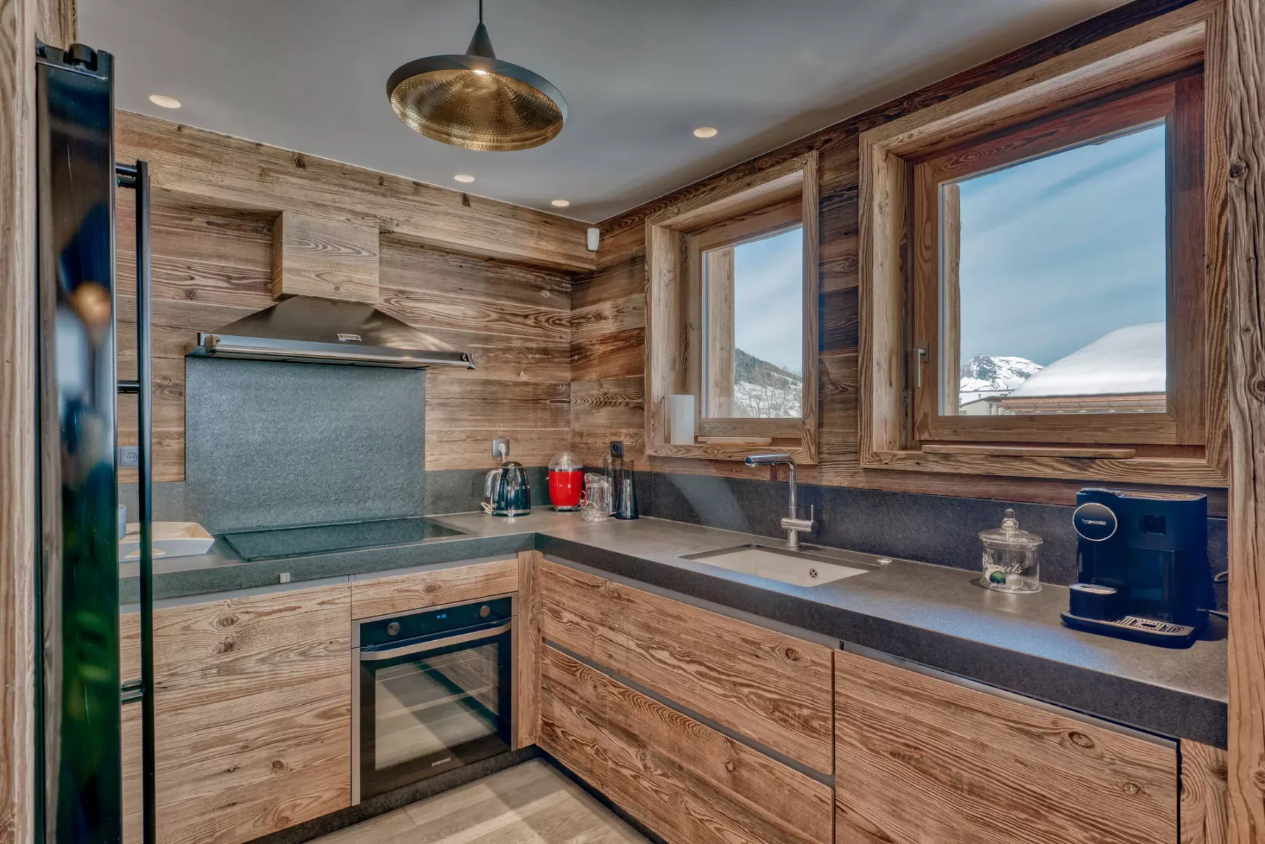 Una cocina revestida de madera con encimera, fregadero y ventanas que dan a un paisaje nevado.