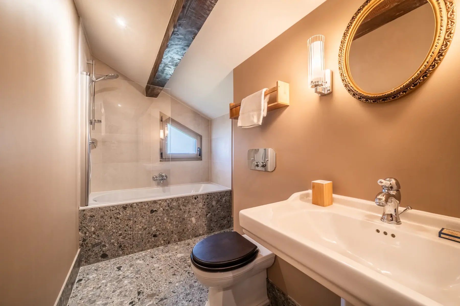 Un baño con bañera, inodoro y lavabo bajo un techo inclinado.