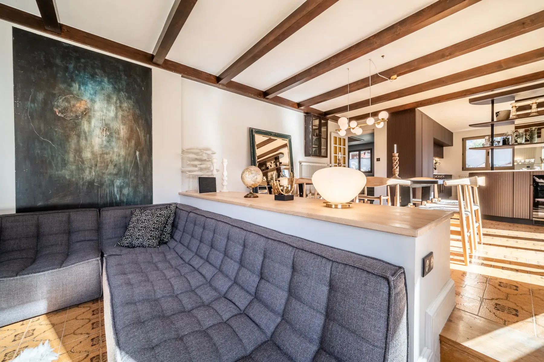 Un salón con asientos grises se abre a una cocina y comedor.