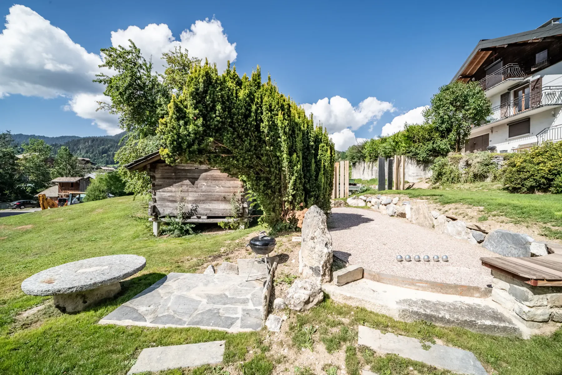 Un jardín ajardinado con un sendero de piedra, una caseta de madera y setos junto a un edificio residencial.