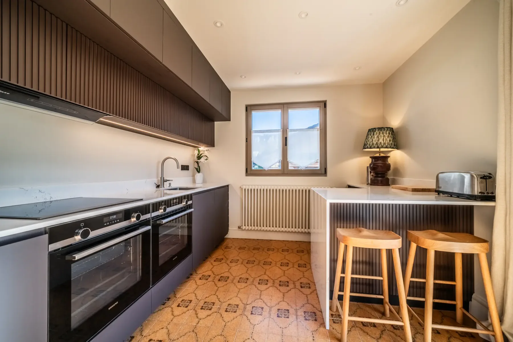 Cocina contemporánea con armarios oscuros, una encimera y una pequeña barra.