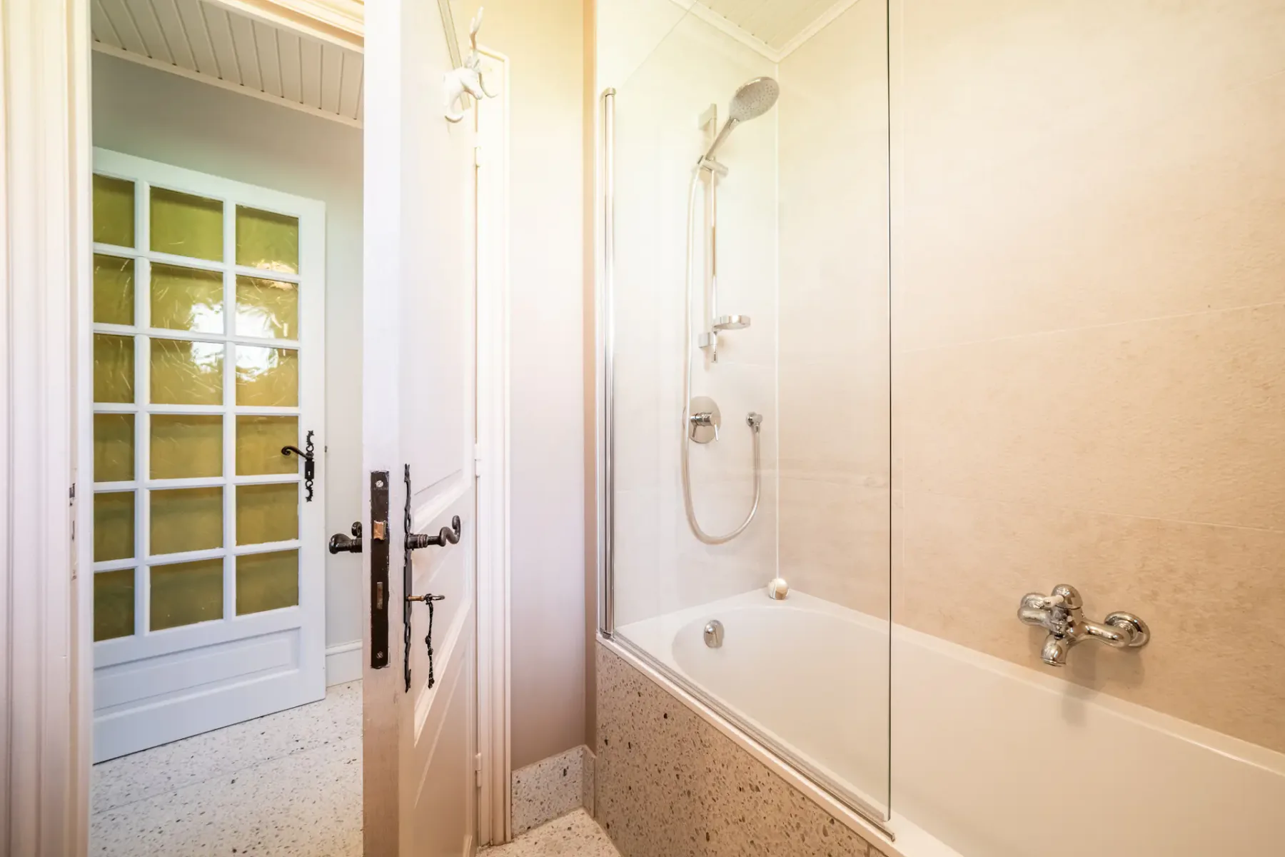 Un baño con bañera y mampara de vidrio junto a una puerta con paneles.