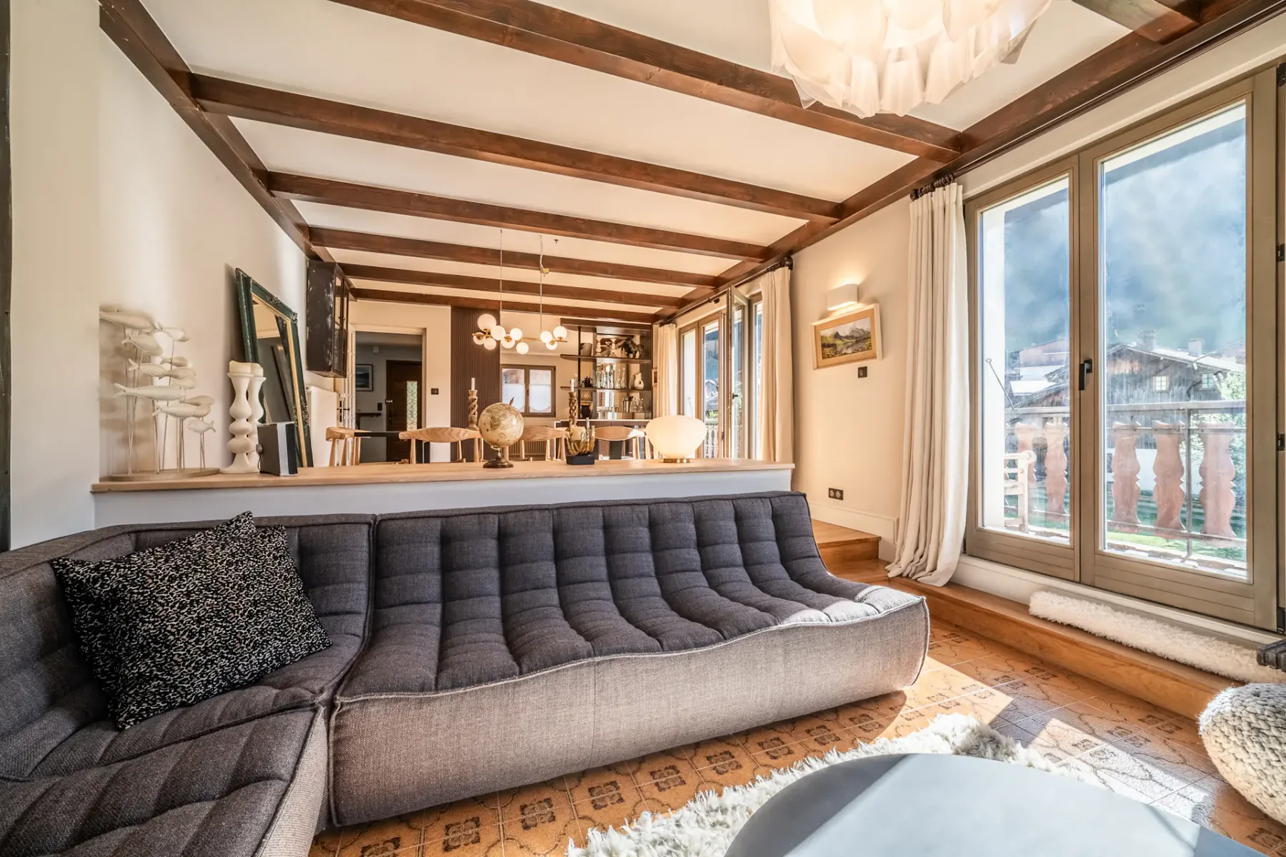 Salón con un sofá gris y grandes ventanales con vistas a las montañas.