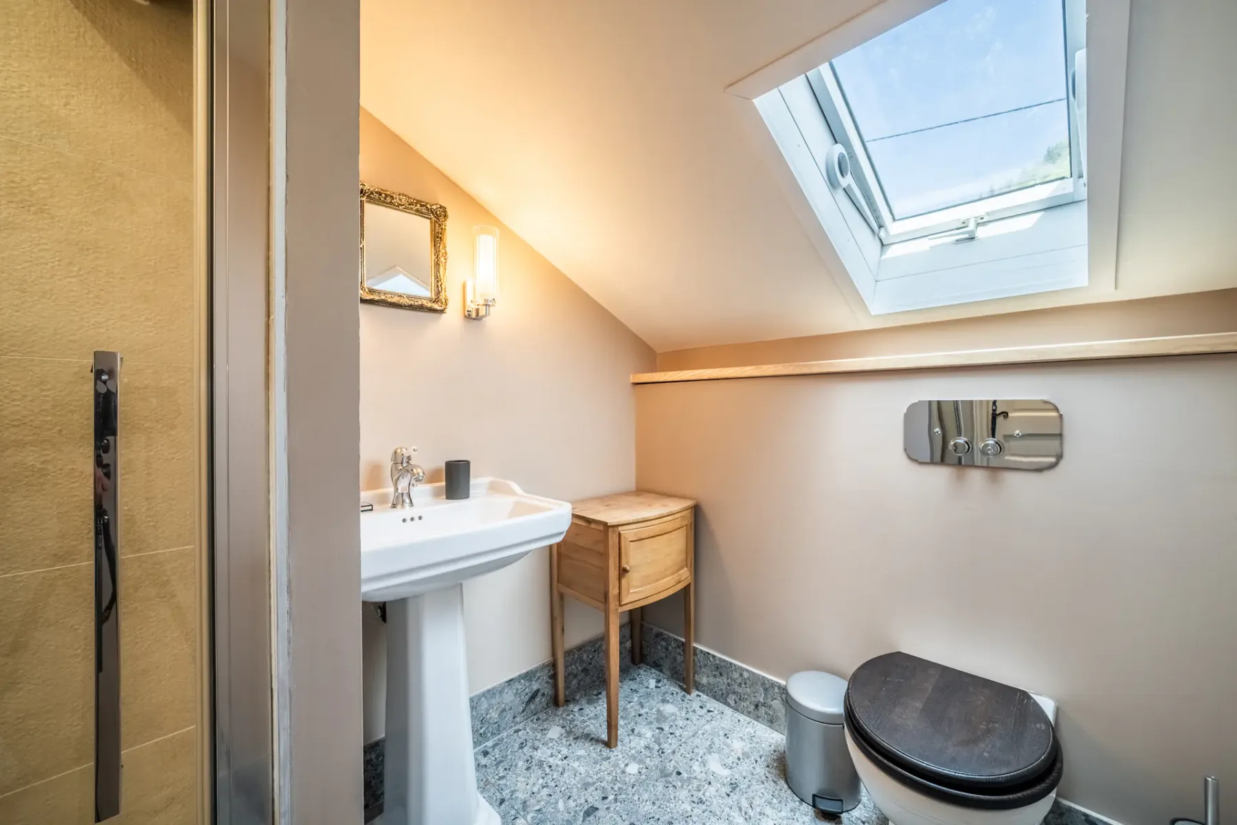 Un baño compacto tiene un lavabo con pedestal, un inodoro y una claraboya.