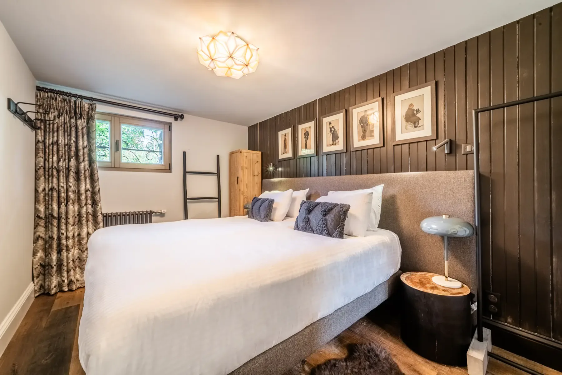 Un dormitorio con una cama grande, cortinas estampadas y cuadros en una pared revestida de madera.