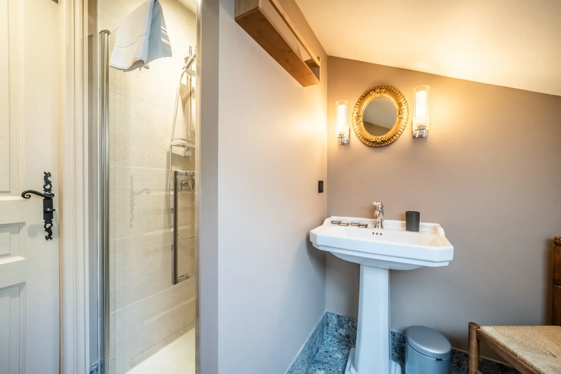 Un baño con lavabo de pedestal, espejo redondo y ducha de vidrio.