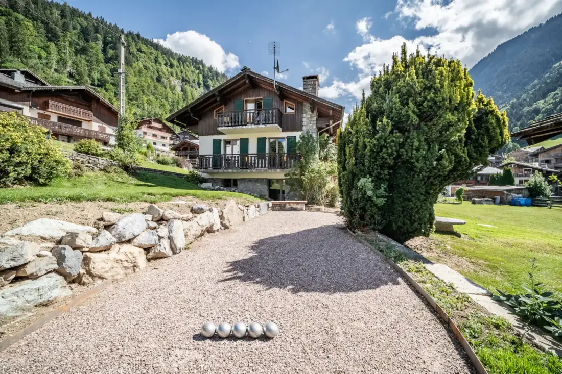 Una zona exterior de grava junto a un edificio tipo chalet, con un muro bajo de piedra.