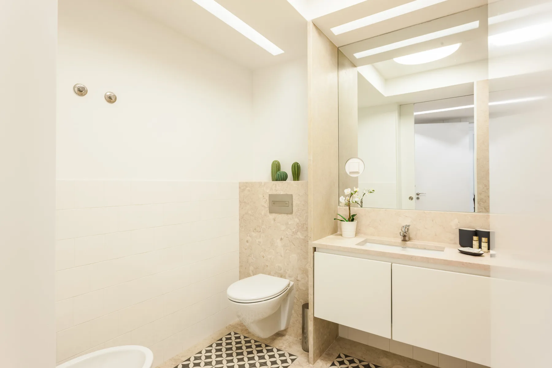 A bright bathroom with a wall-mounted toilet and a vanity beneath a large mirror.