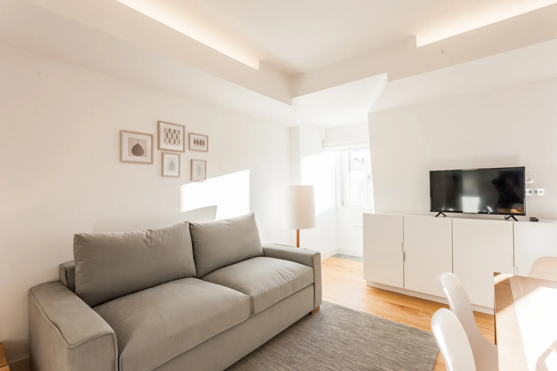 A bright living room with a gray sofa, framed pictures, and a television.