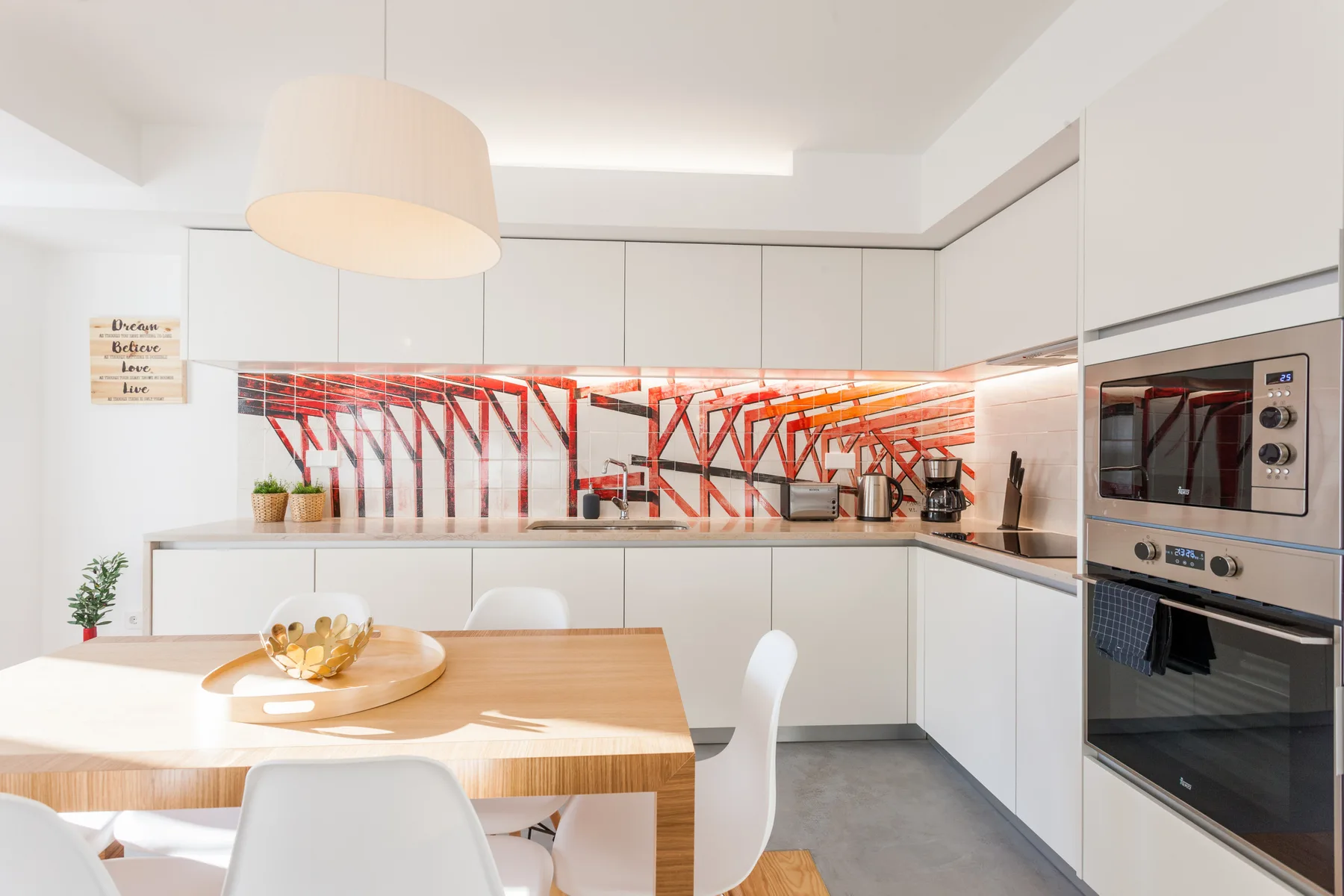 A bright modern kitchen and dining area with white cabinetry and a wooden table.