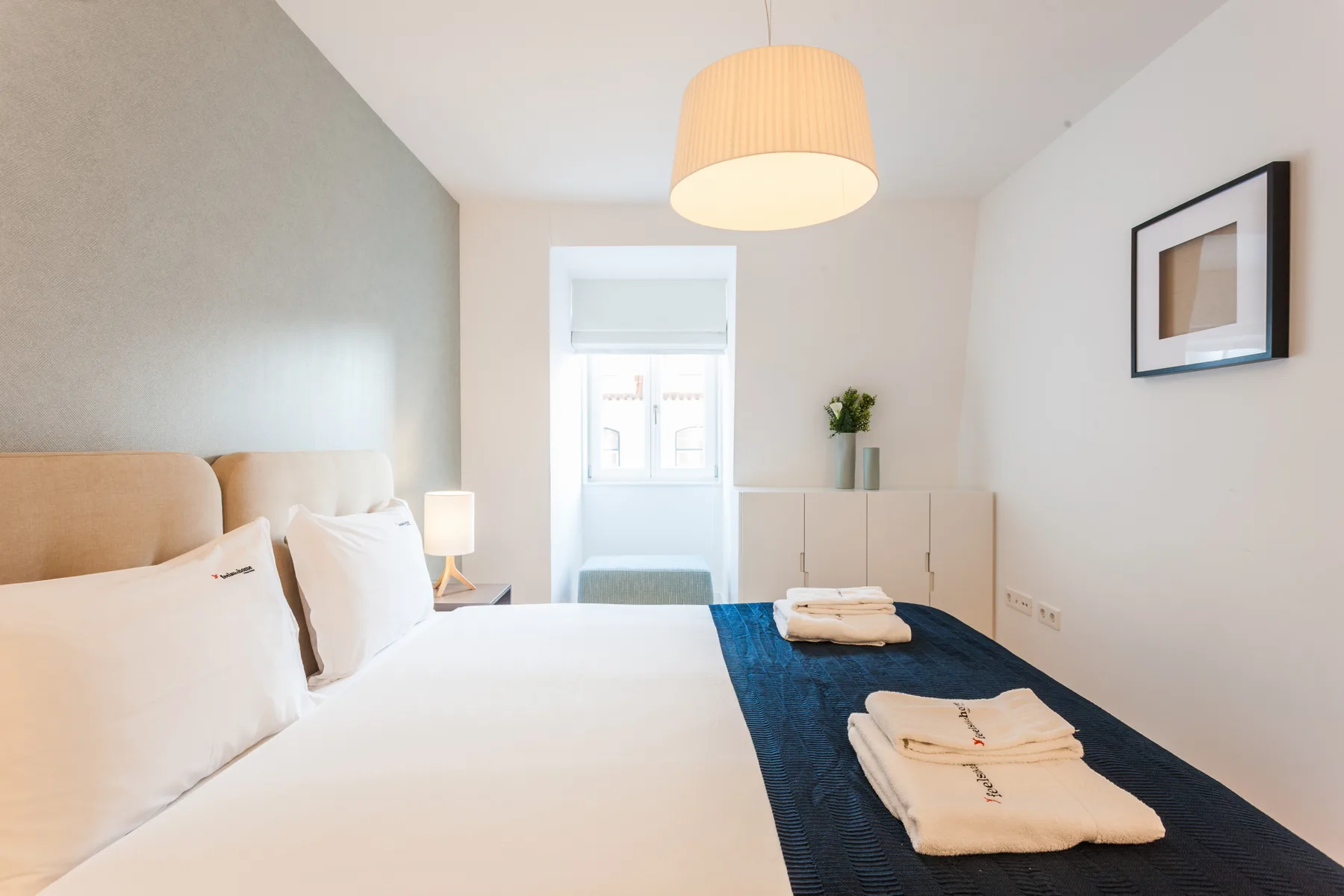 A bright bedroom with a bed, folded towels, and a window.