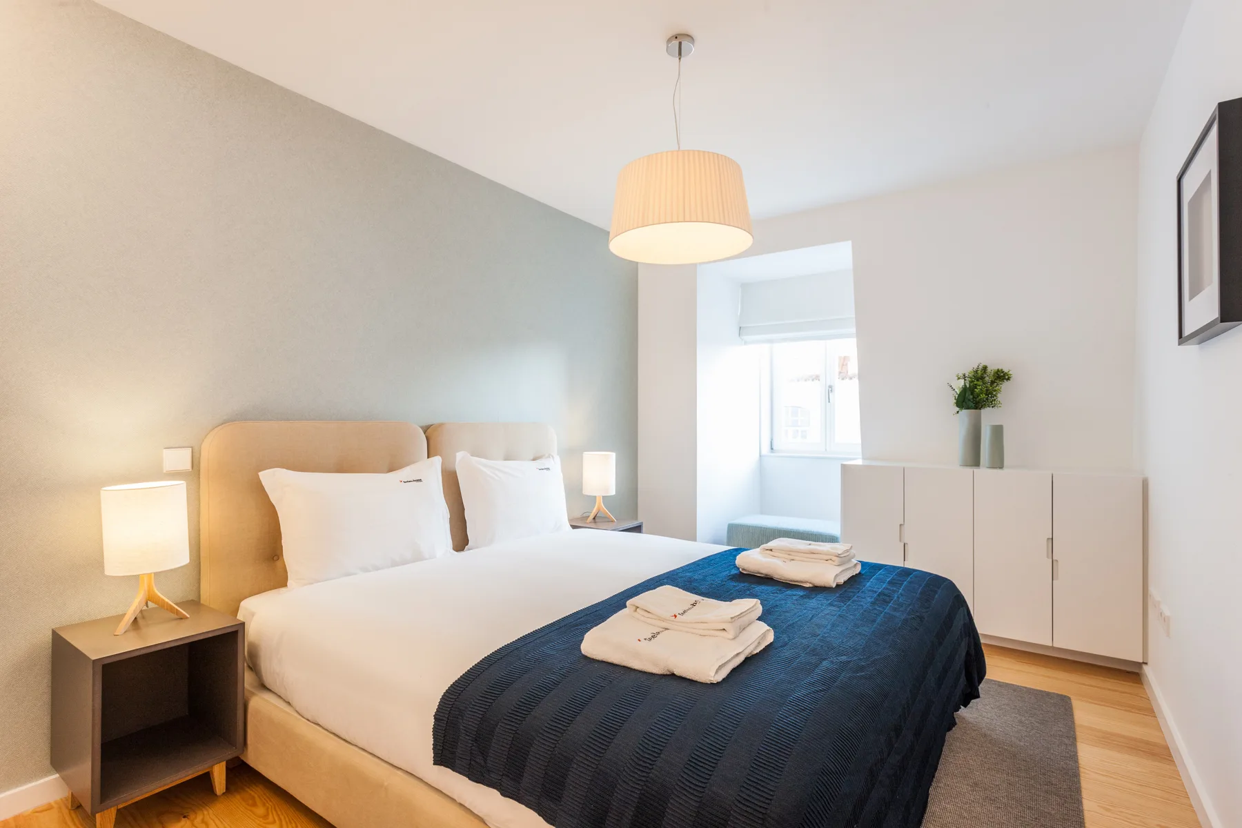 A bright bedroom with a neatly made bed and bedside lamps.