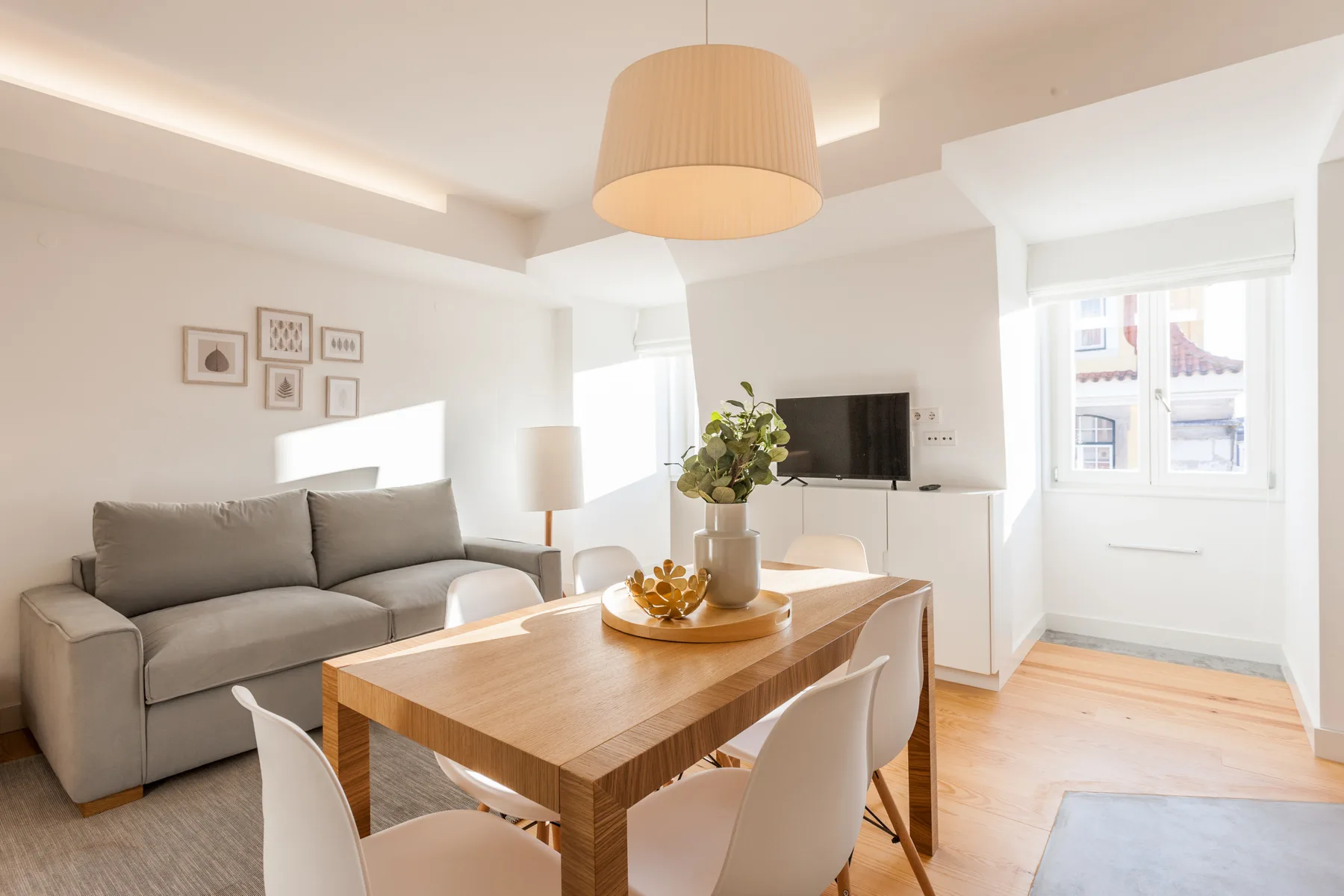 A bright living and dining area with seating, a wooden table, and large windows.