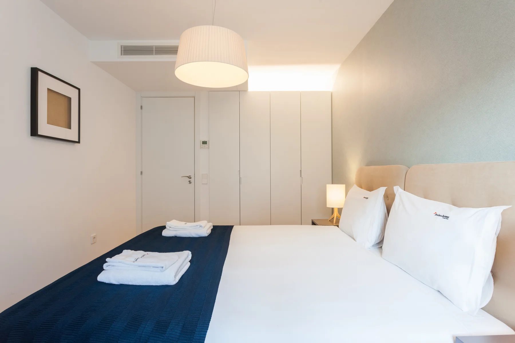 A bright bedroom with a neatly made bed and folded towels.