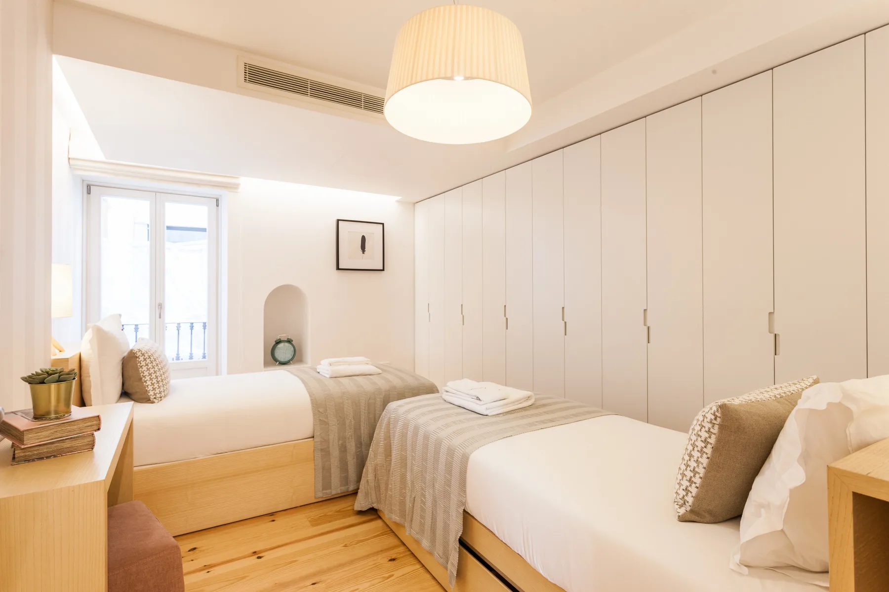 A bright bedroom with two beds and built-in wardrobes.