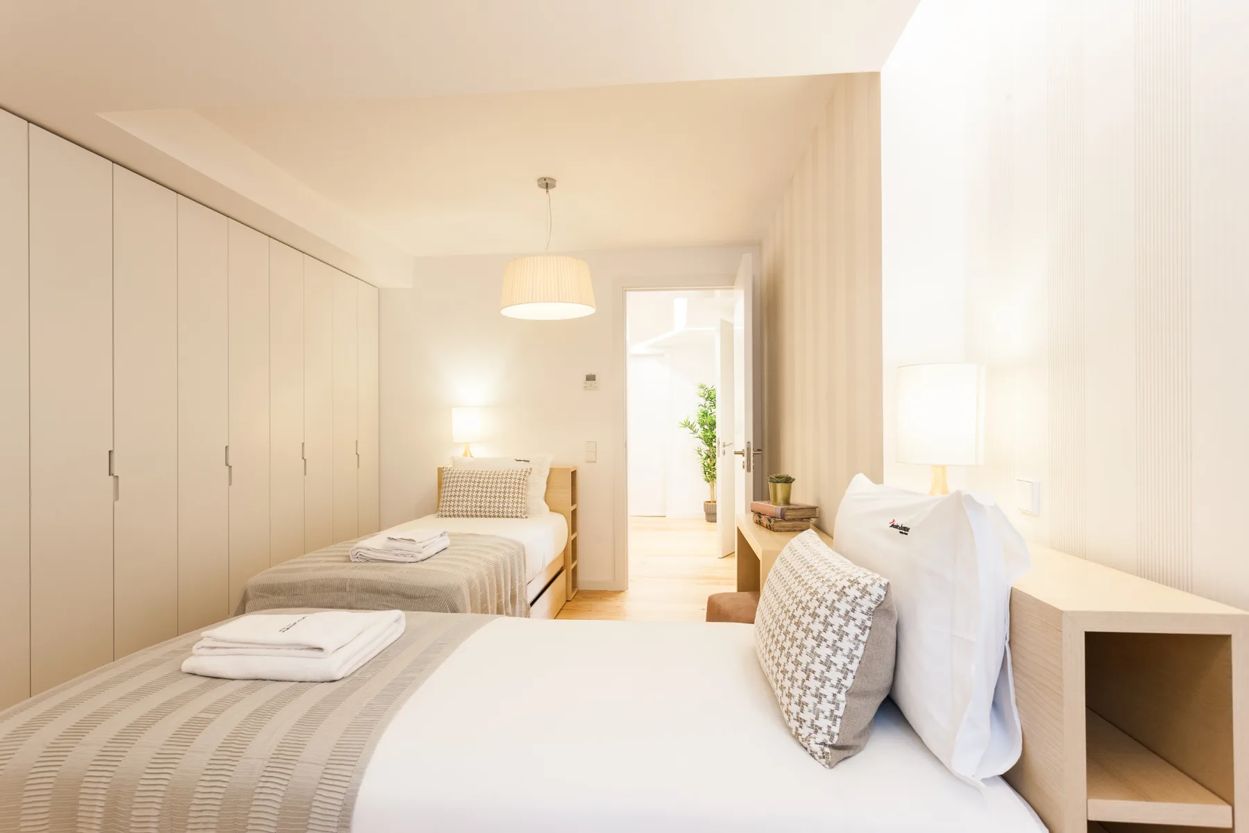 A bright bedroom with two beds and built-in wardrobes along one wall.