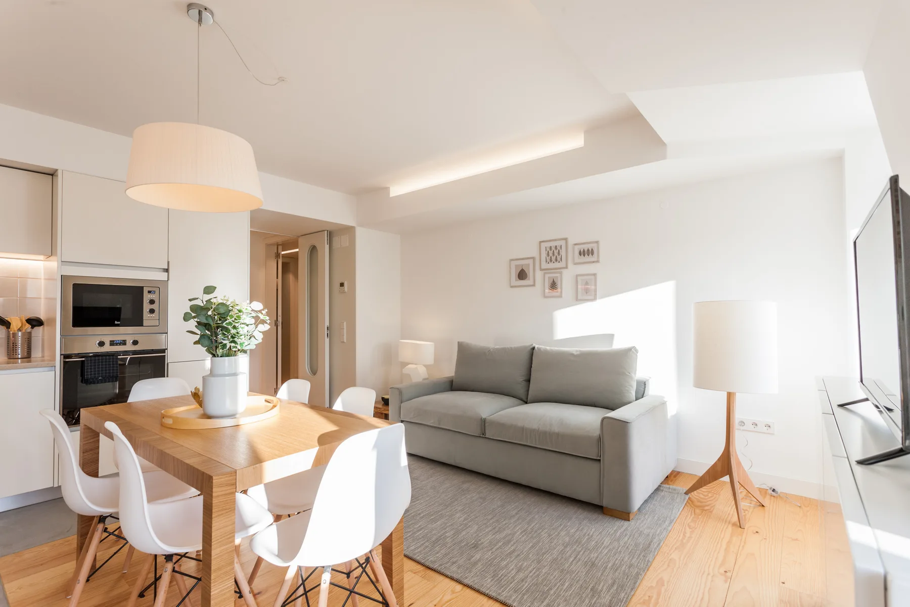A bright living and dining area with a gray sofa and wooden table.
