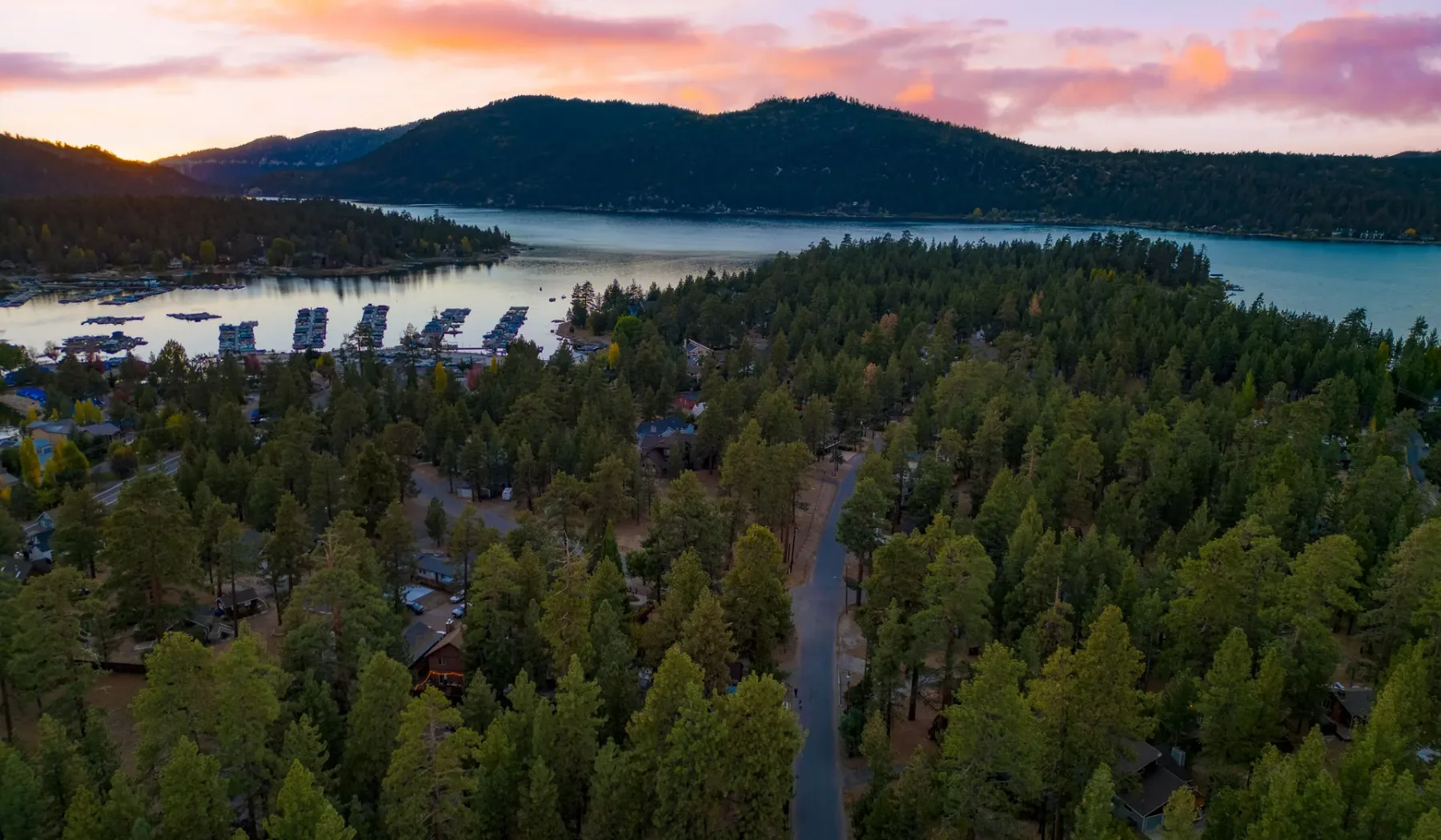 Aerial view of a wooded lakeside settlement beneath a colorful sunset sky.