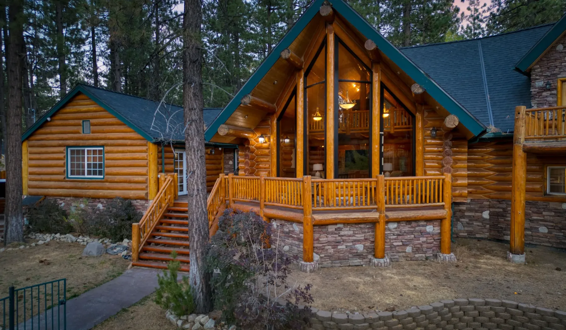 A large log cabin with a covered porch and tall central windows stands among trees.