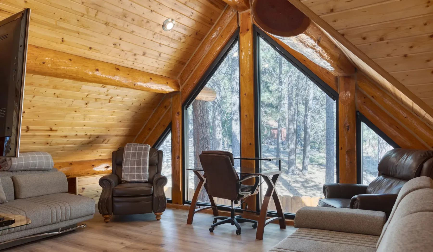 A-frame living room with seating beside large windows overlooking trees.