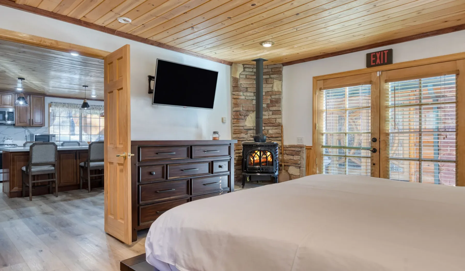 A bedroom with a bed, dresser, television, and wood-burning stove.