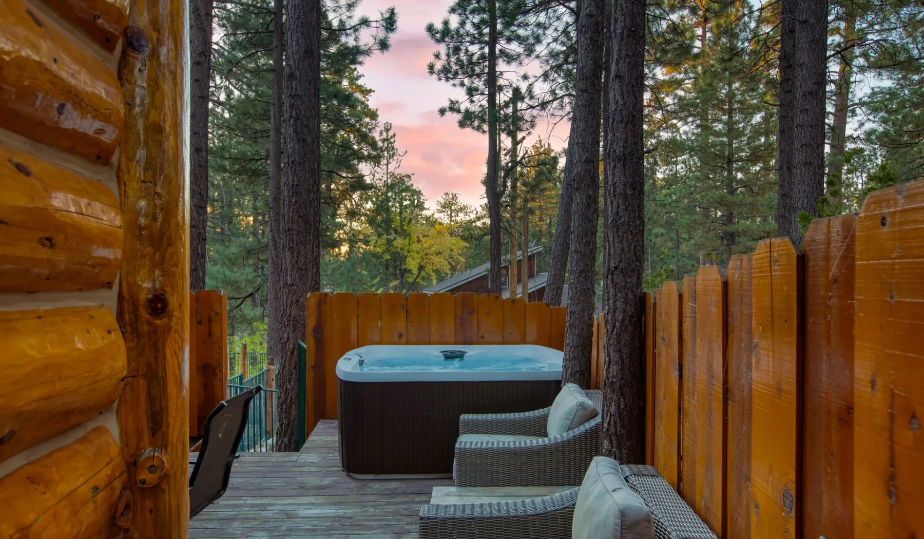 A deck with an outdoor hot tub and seating overlooks a wooded landscape.