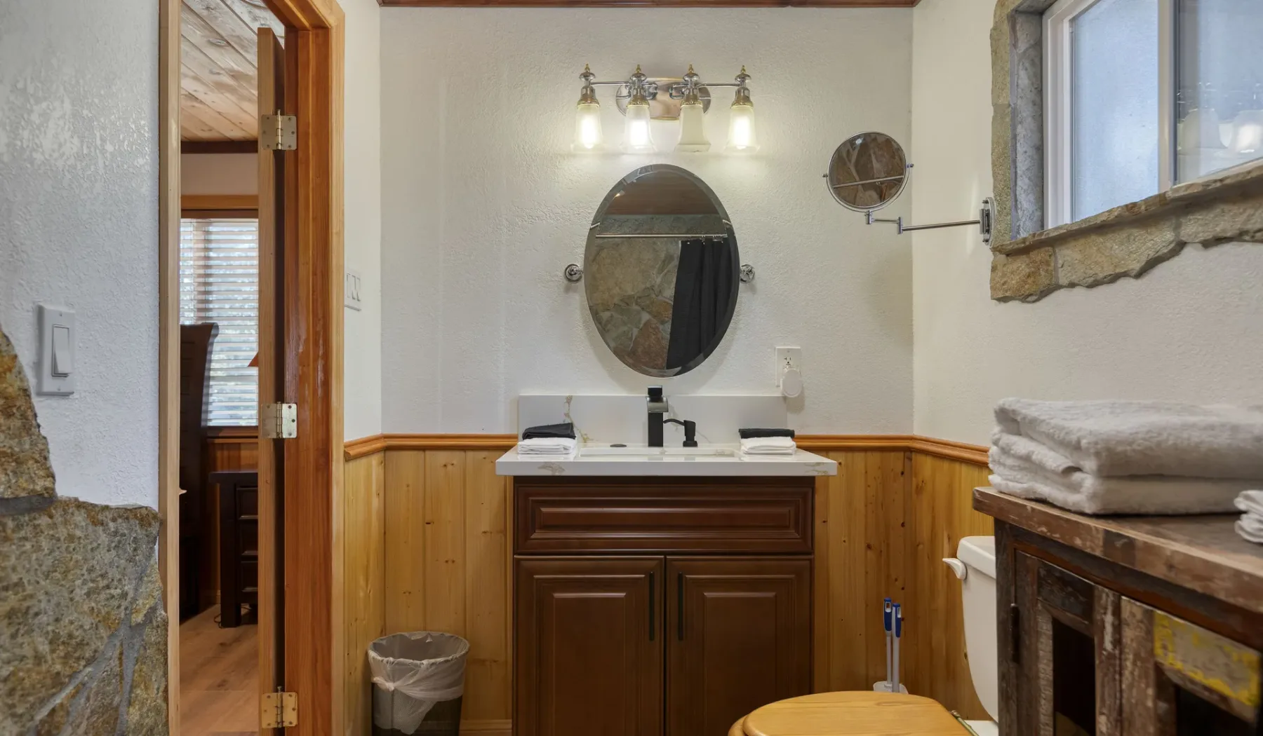 A bathroom vanity with an oval mirror and a window beside the sink.