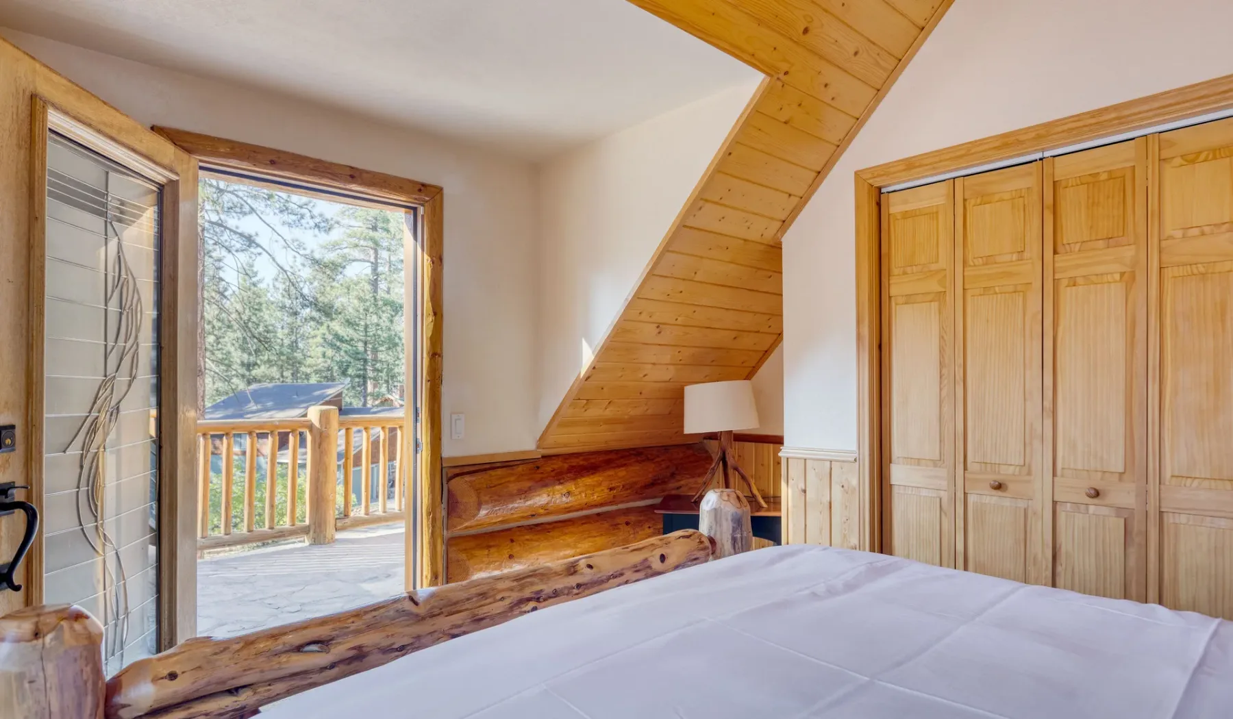 A bedroom with a bed, wooden closet doors, and a sloped wood ceiling.
