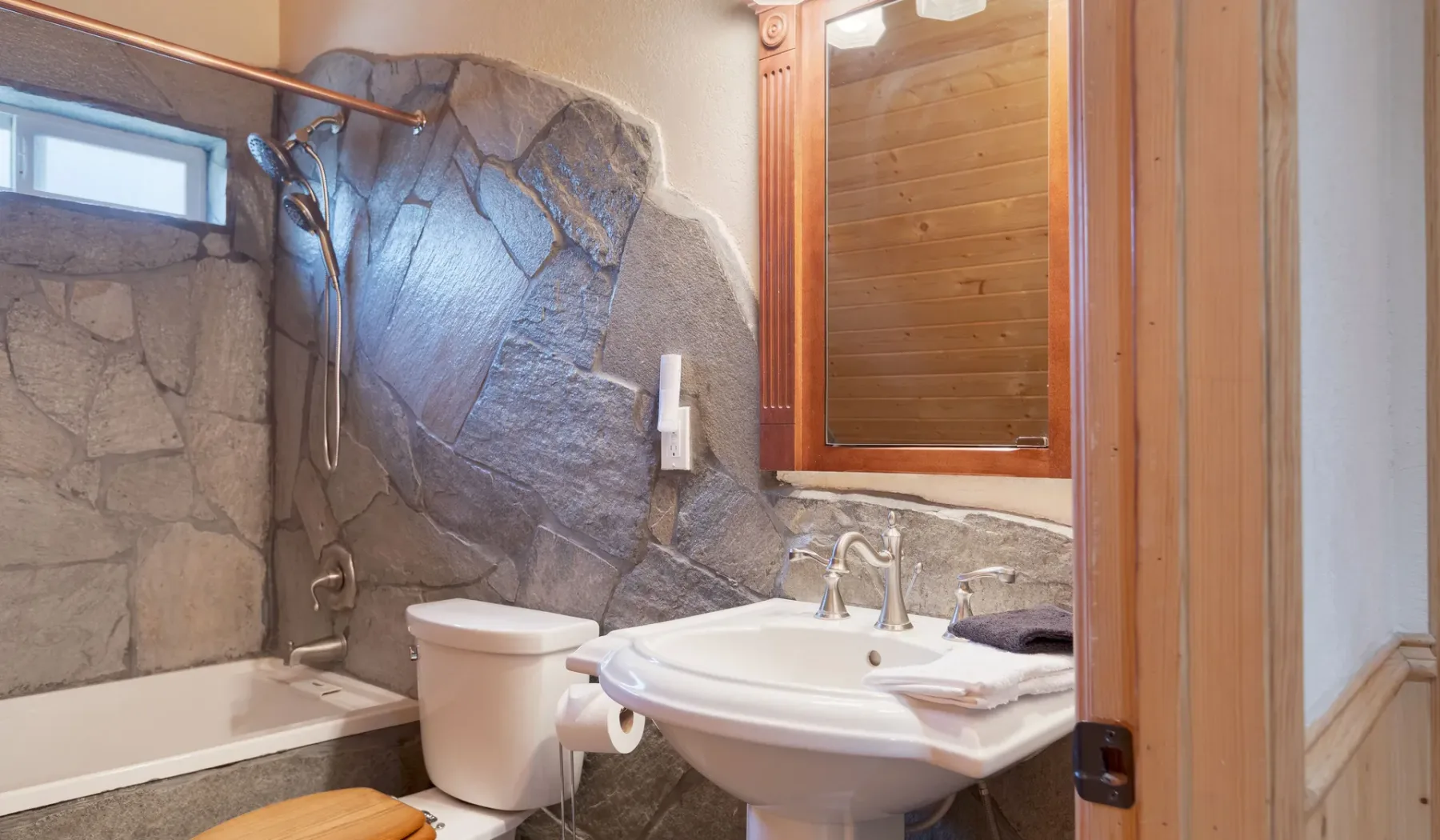 A bathroom with a bathtub, toilet, and sink against a stone wall.