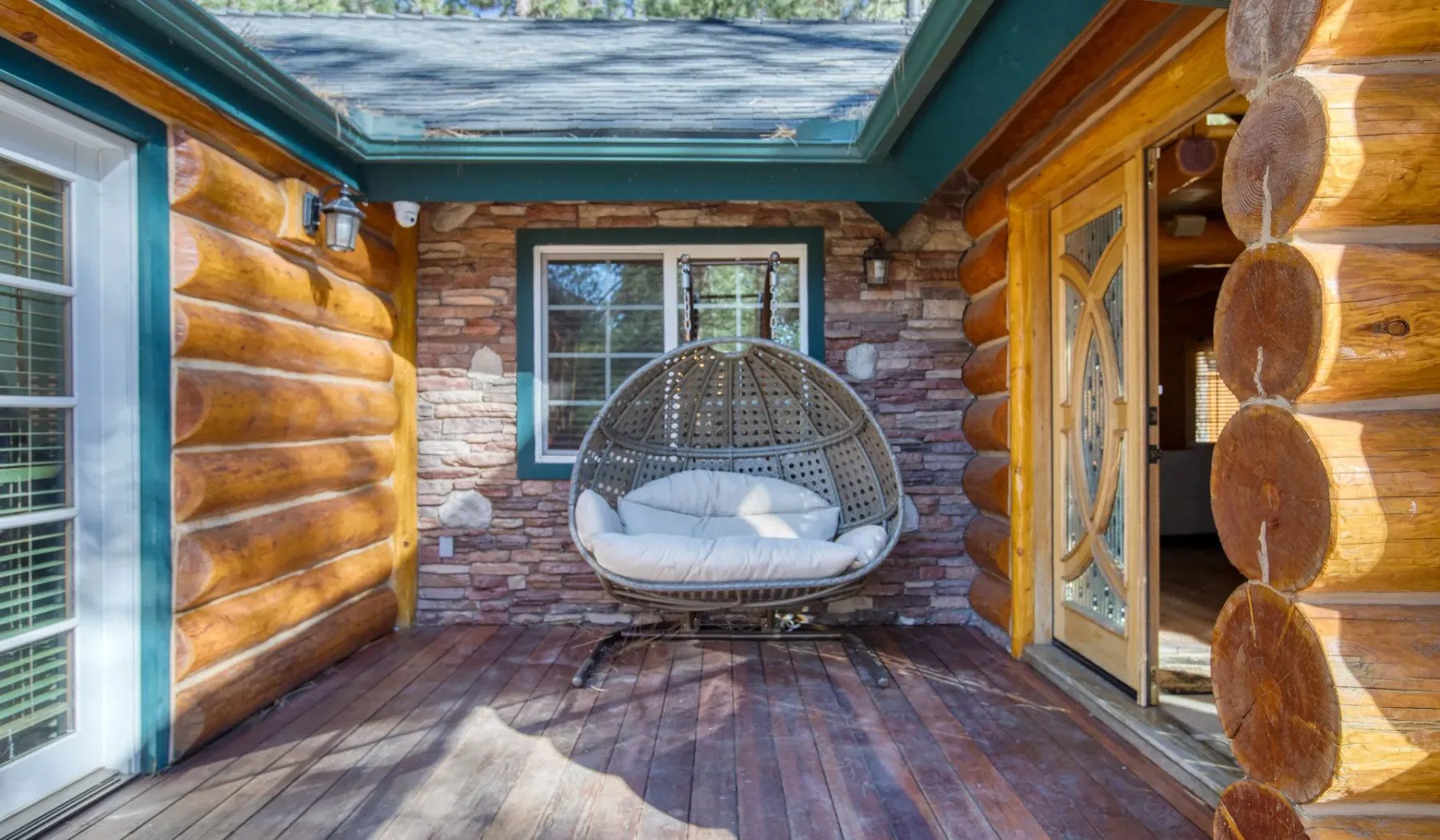 A covered log-wood porch features a hanging cushioned seat and a window.