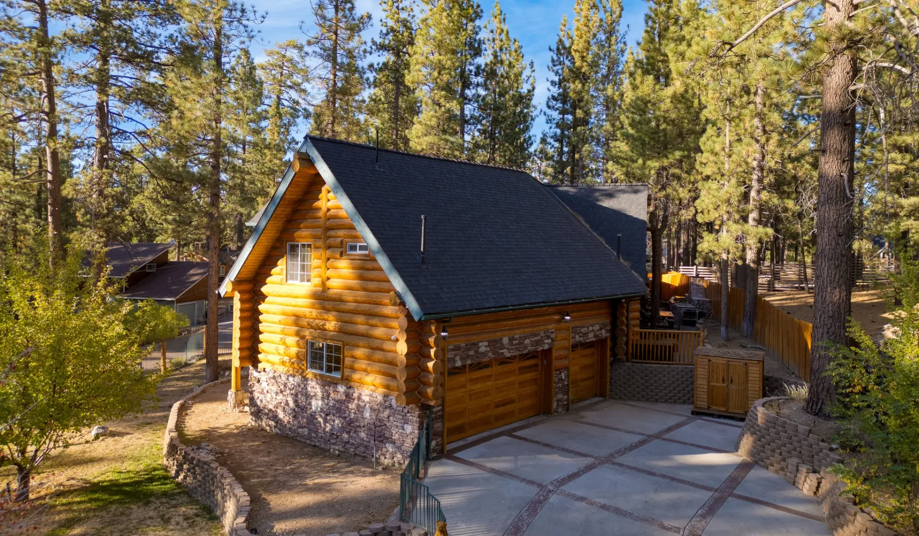 A log cabin with a dark roof sits among tall pine trees.