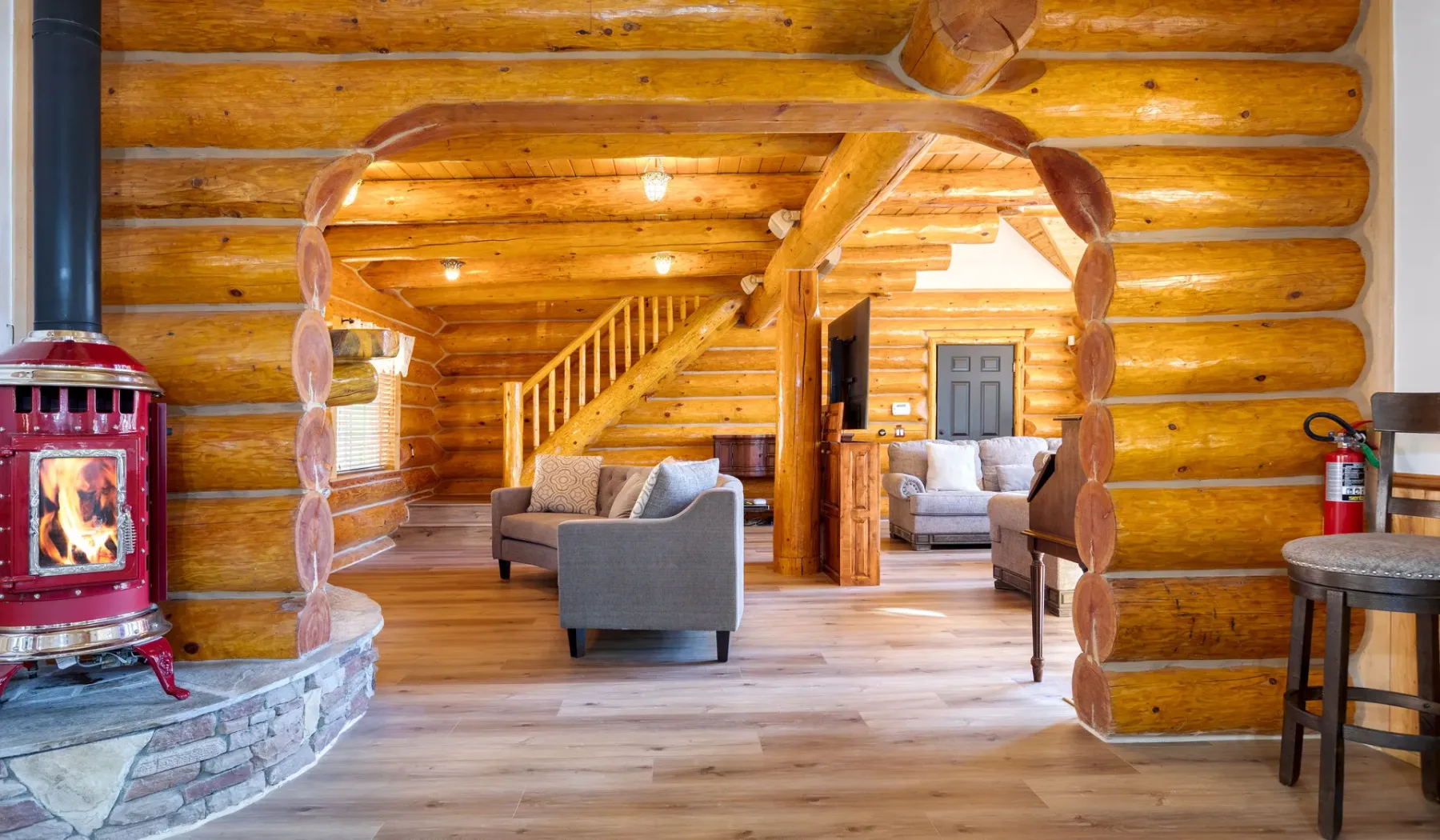 A log cabin living room with seating, a staircase, and a wood-burning stove.