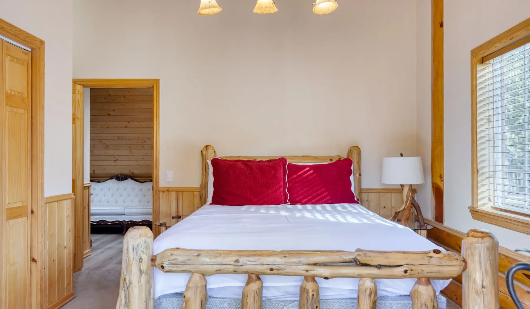 A bedroom with a log bed, white bedding, and red pillows.