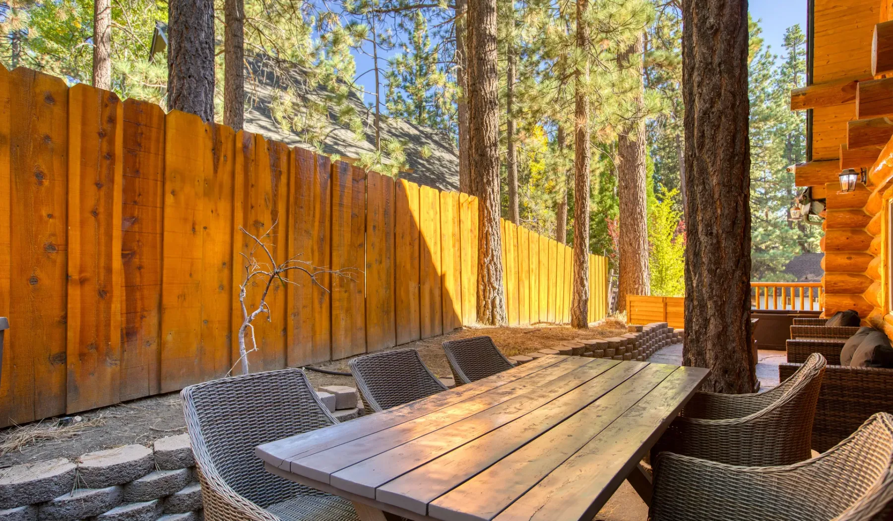 An outdoor dining area with a wooden table and seating beside a forest.