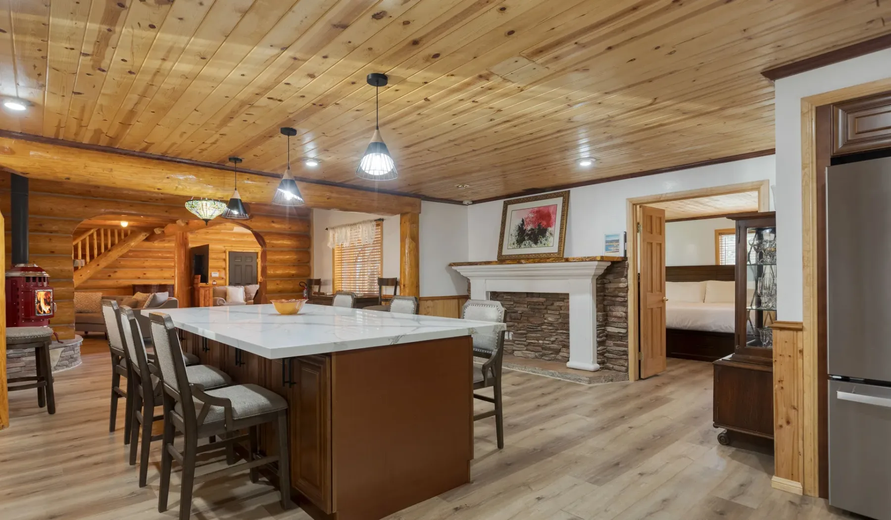 A dining area with a large table sits beneath a wood-paneled ceiling.