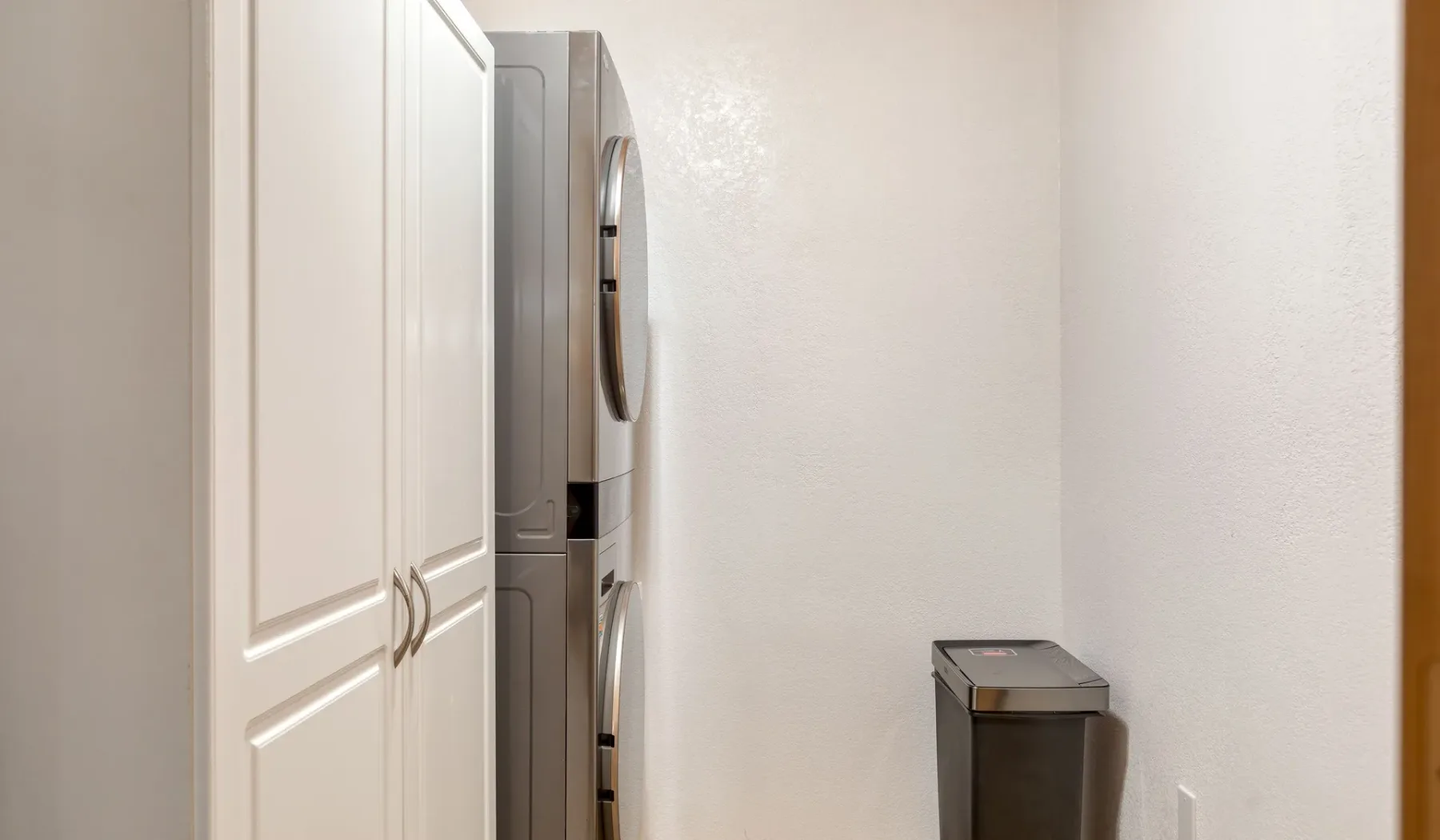 A laundry area with stacked appliances beside white cabinets.