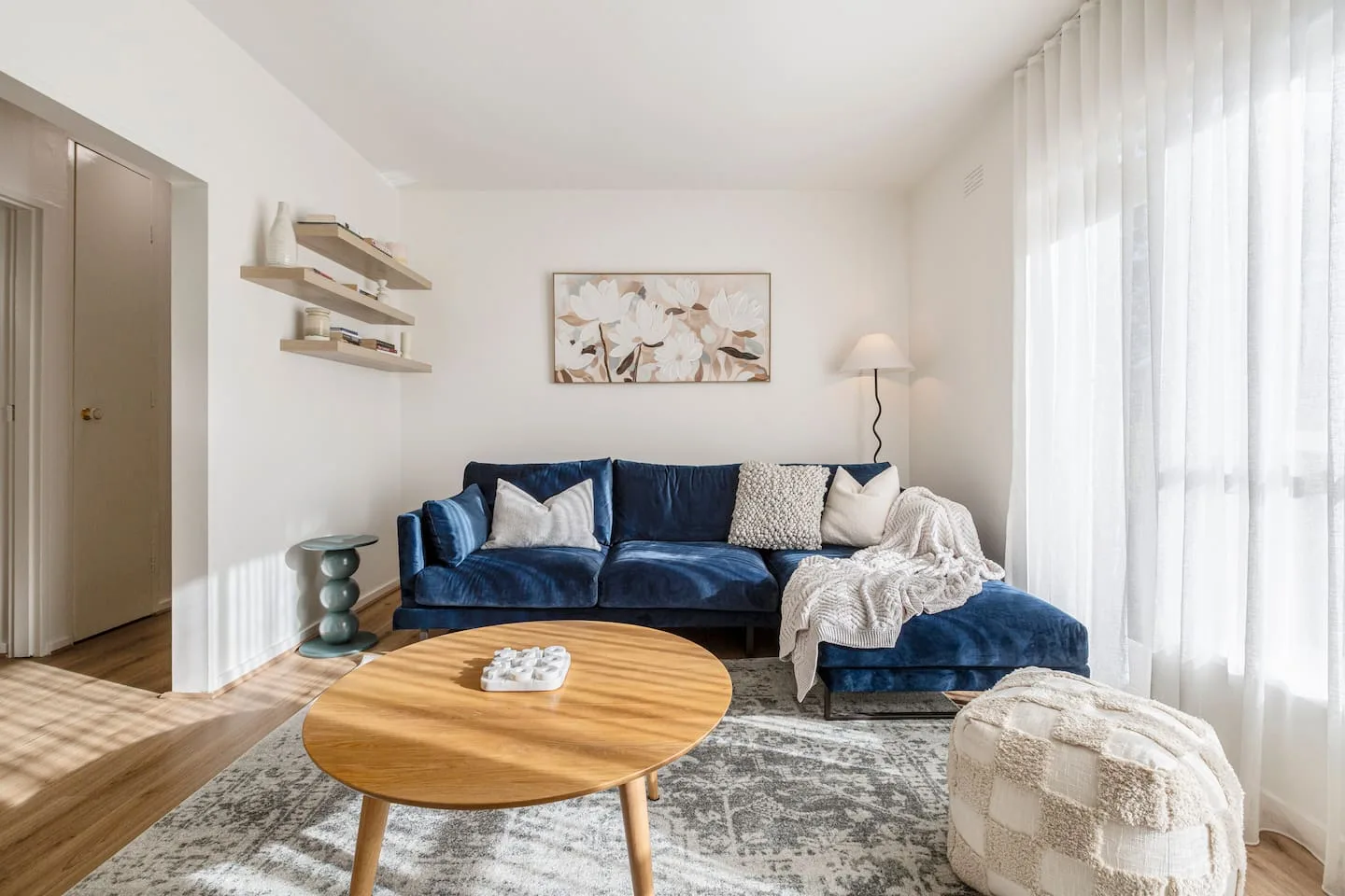 Una sala de estar luminosa con asientos azules, una mesa de centro de madera y cortinas translúcidas.