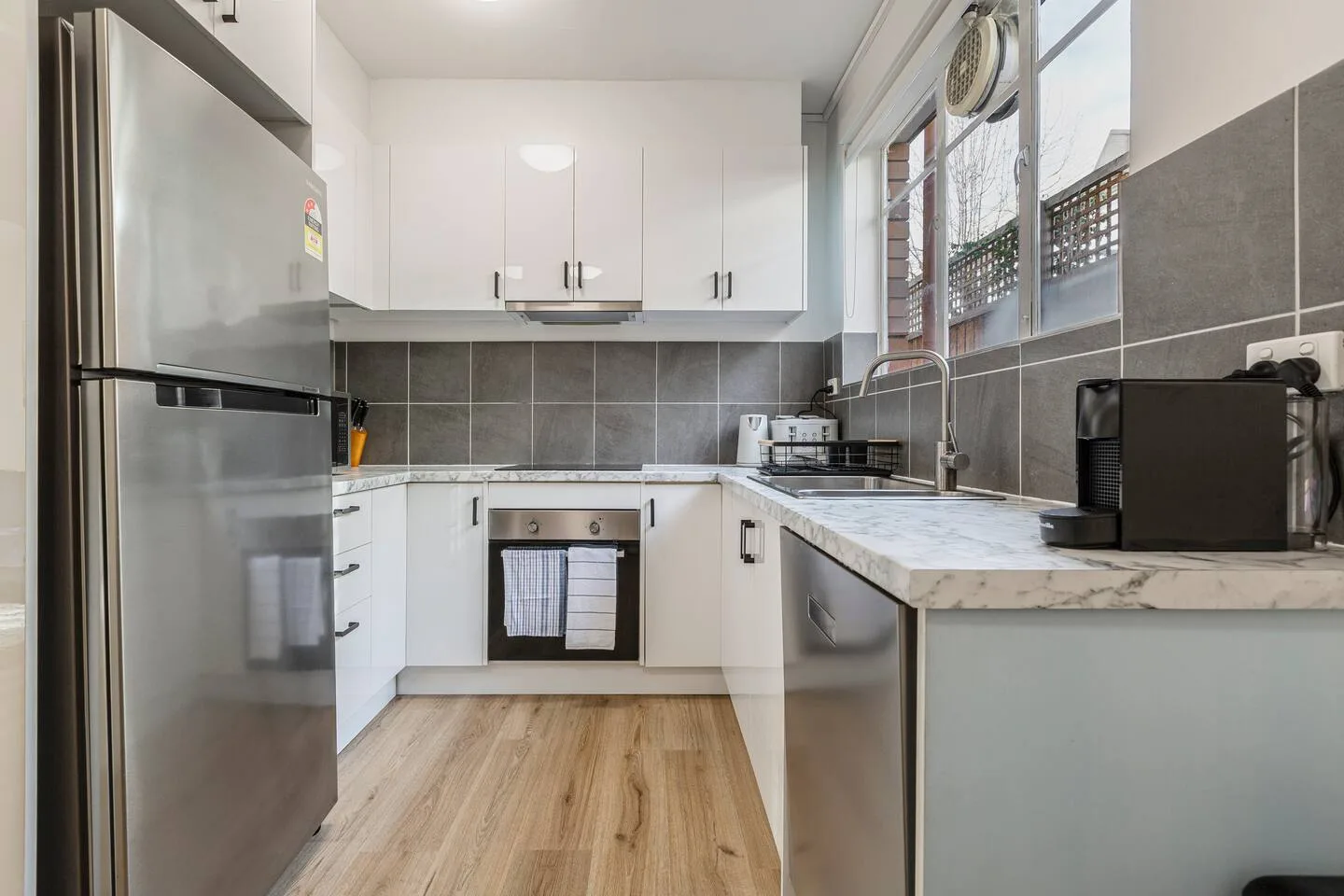 Prepare meals with ease in the modern kitchen featuring marble-look benches, a full-size fridge, an oven, and a stovetop.