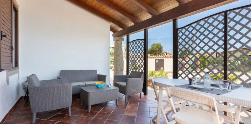 A covered patio with seating and a dining table beneath a wooden roof.