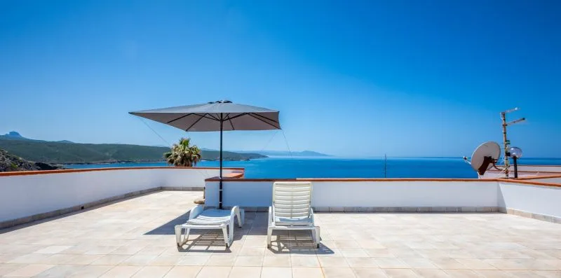 A rooftop terrace overlooks the sea, with seating beneath a large umbrella.